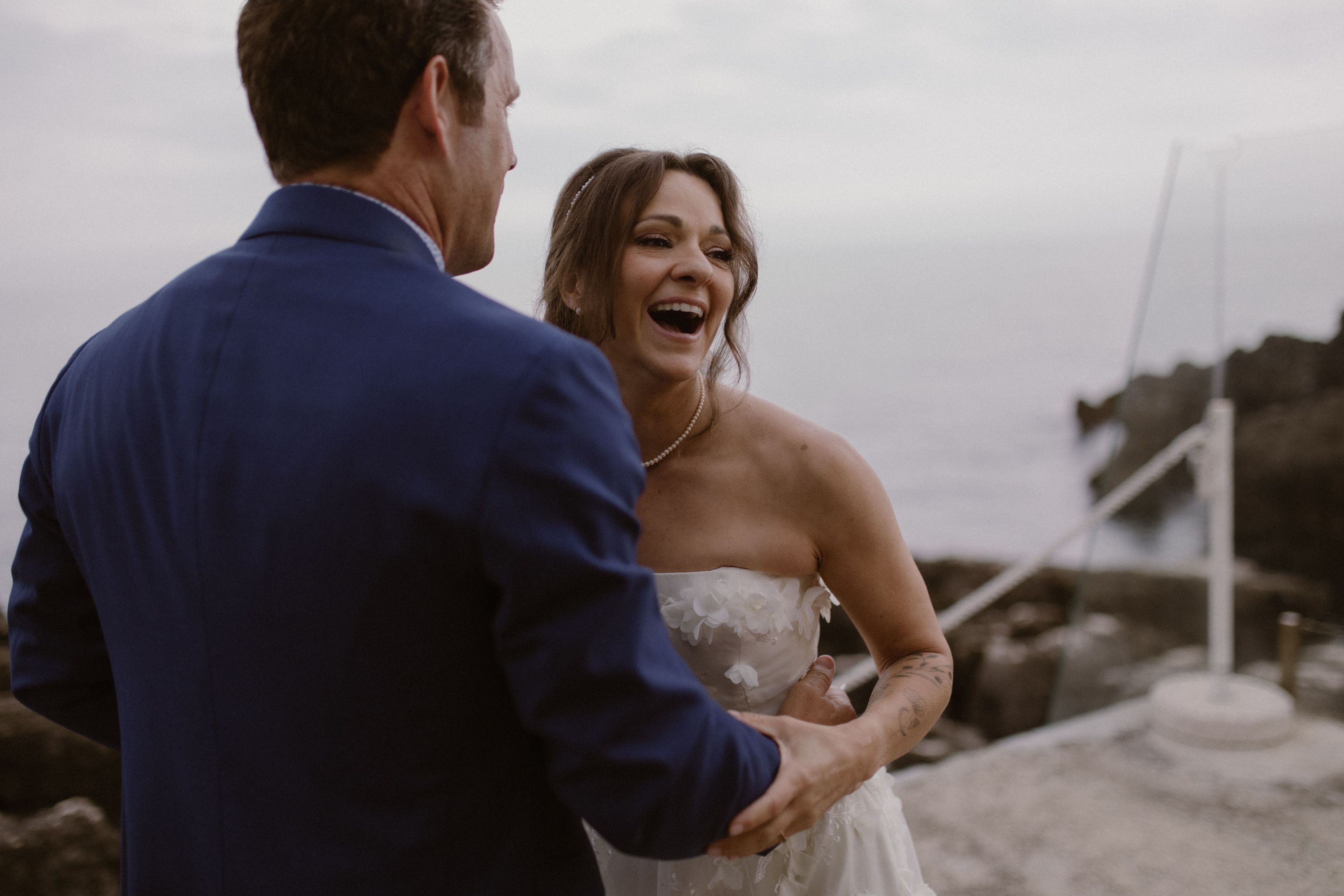 Bride laughing while holding her groom with the ocean in the background during their destination elopement in Portugal