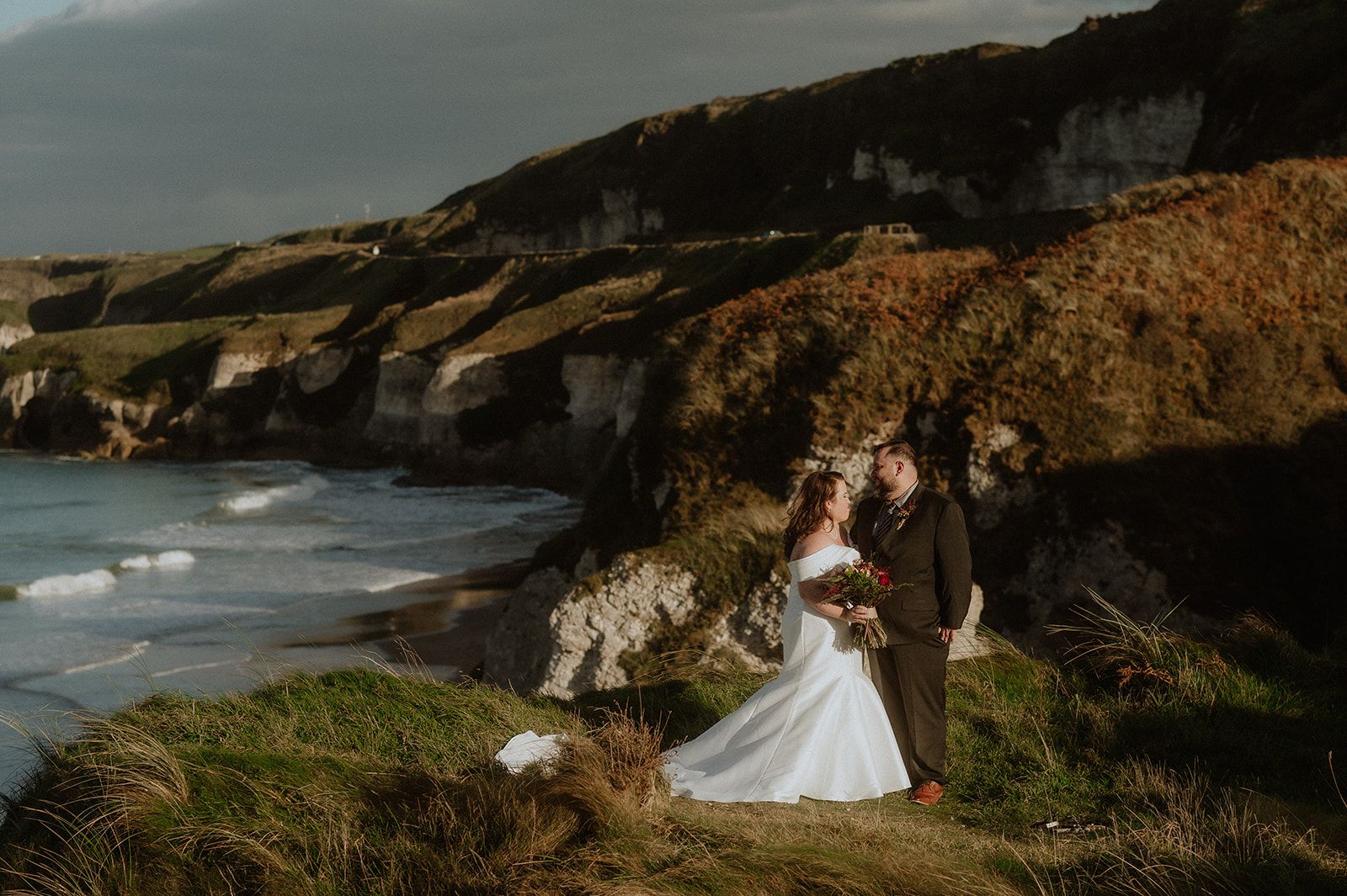 Wide shot of bride and groom with the cliffs, meadows, and lush Antrim landscapes during their elopement in Ireland