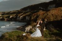 Wide shot of bride and groom with the cliffs, meadows, and lush Antrim landscapes during their elopement in Ireland