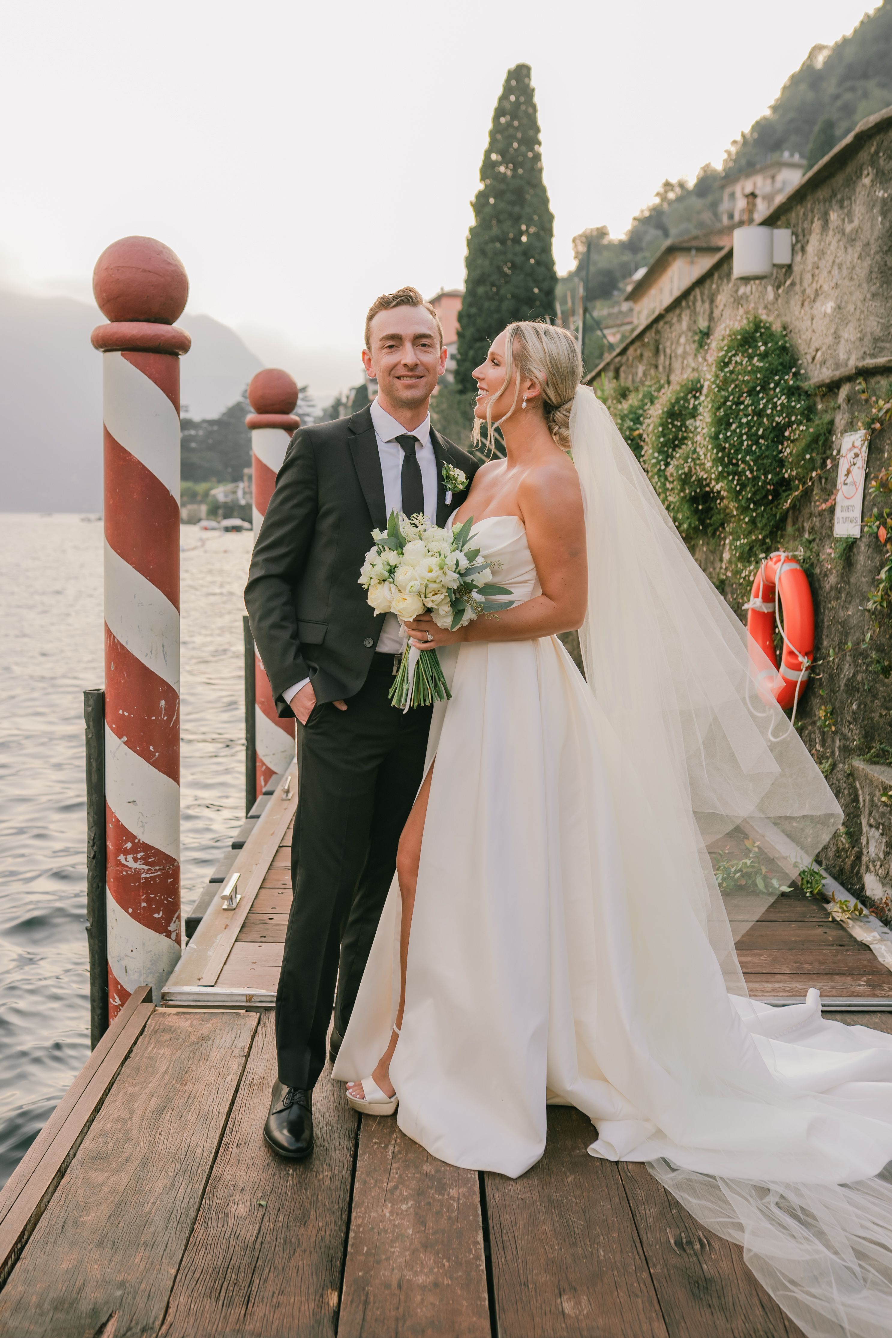 Groom looks at the camera as the bride looks at him during their romantic Lake Como photoshoot for their vow renewal in Italy