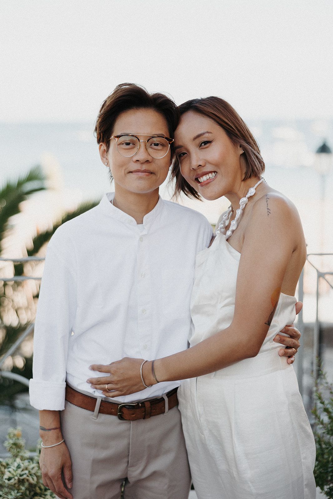 Newlyweds hugging and looking at the camera with a palm tree behind in a photoshoot during their destination wedding in Portugal