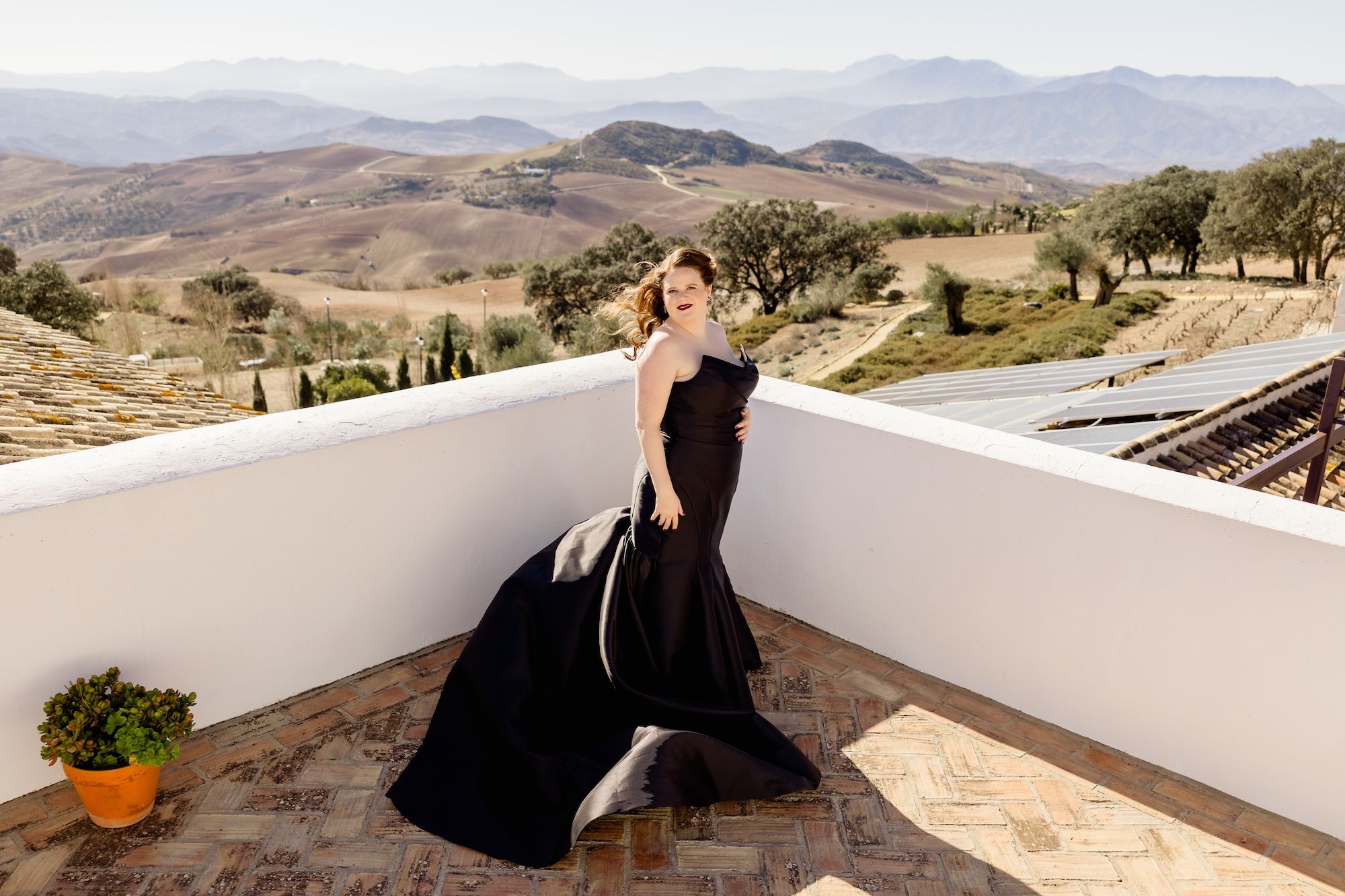 Bride in black wedding dress stands on a terrace overlooking Antequerra, Spain’s lush green and mountainous landscape