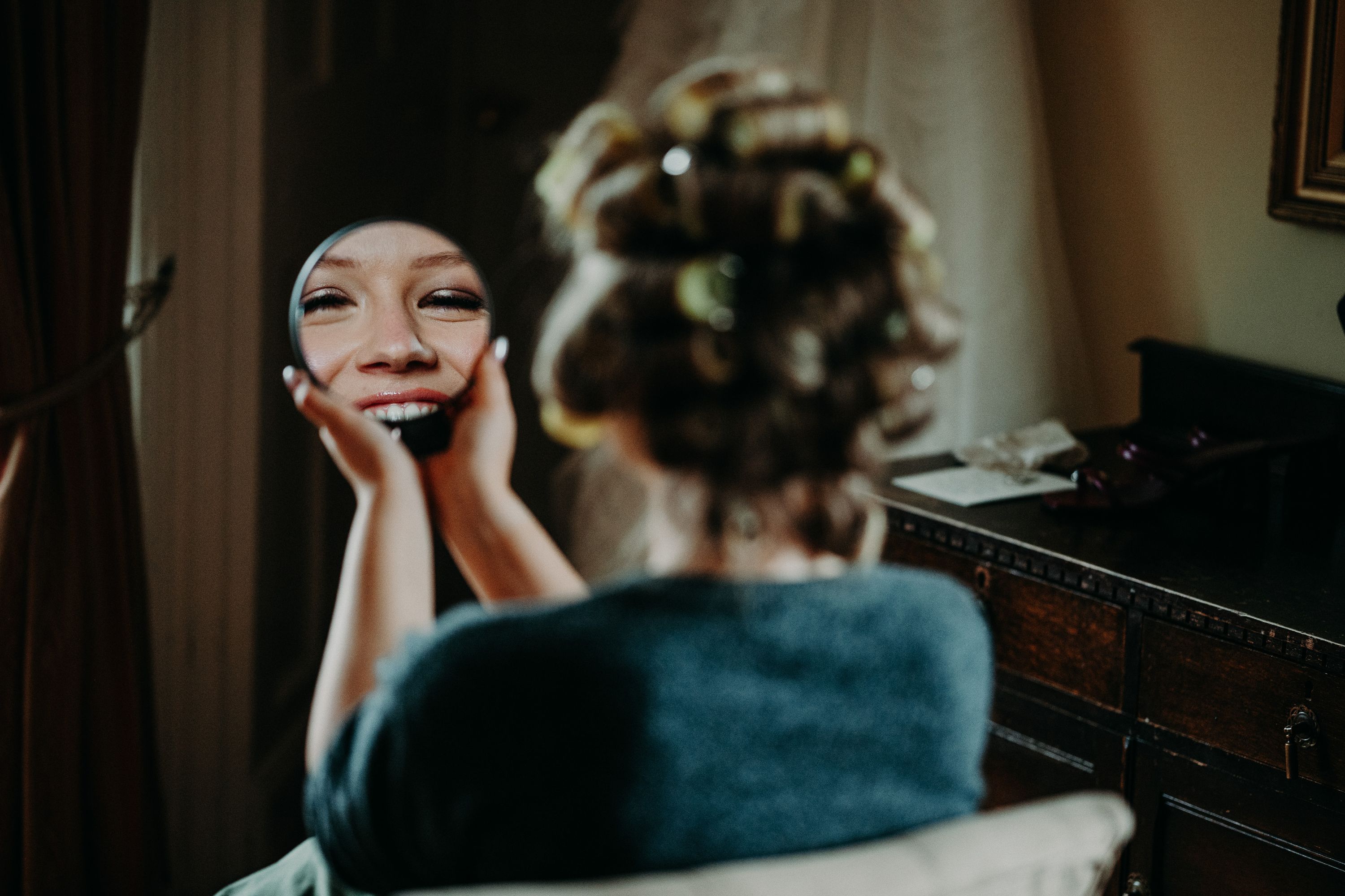 Bride smiling into a handheld mirror while getting ready for an intimate wedding in Ireland