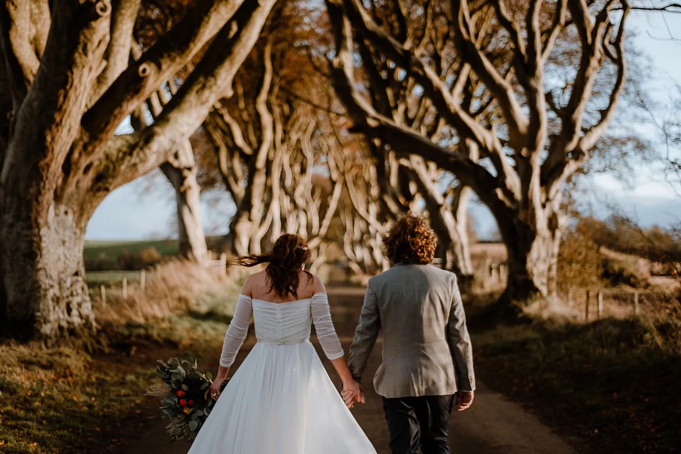Bride and groom walking on the path of the Dark Hedges with beech trees lined up on the side of the road