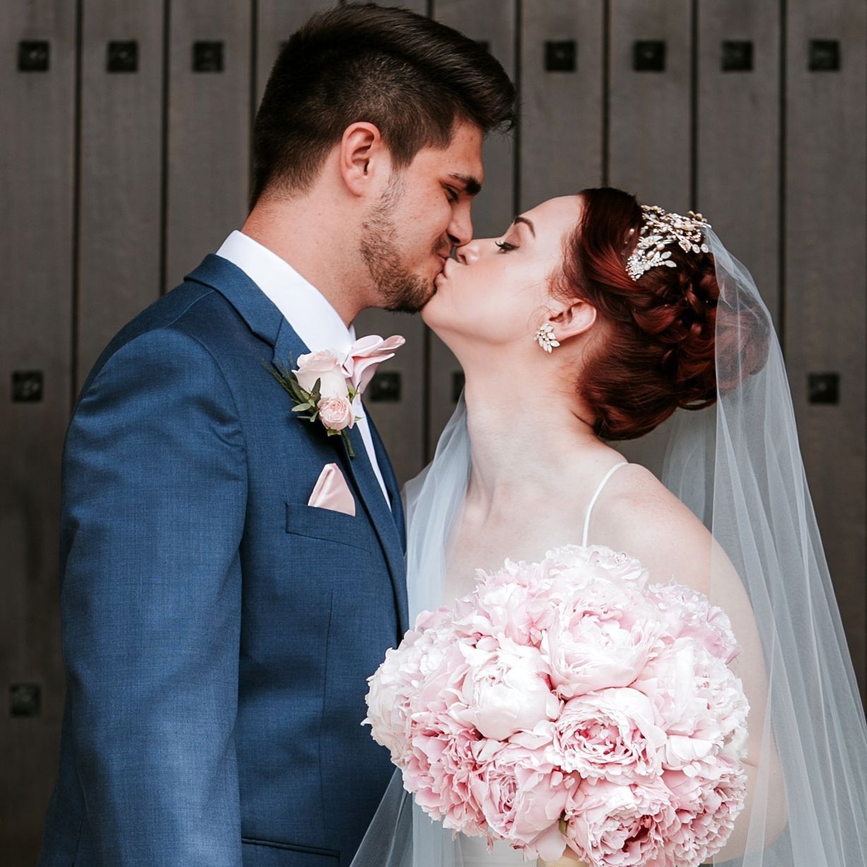 Bride and groom sweetly kissing each other while the bride holds her bouquet made of big pink peonies