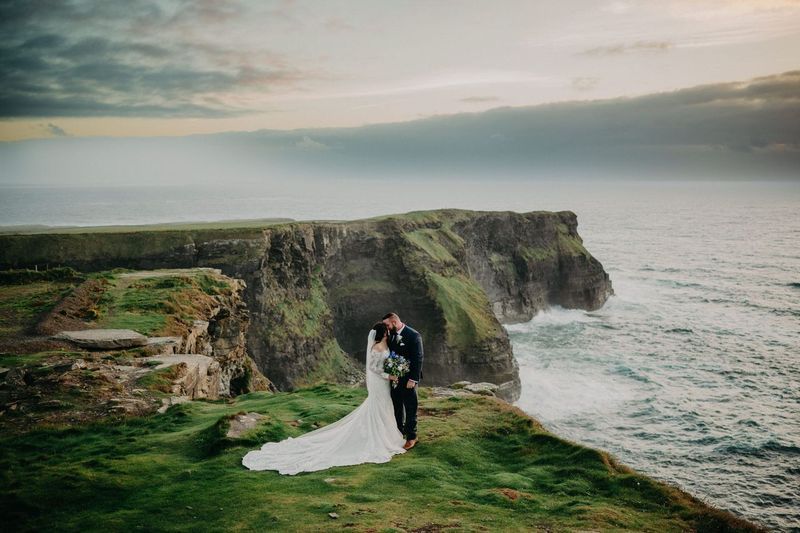 Newlyweds on the cliffs kissing during their elopement in Ireland with the Cliffs of Moher and Atlantic Ocean as the backdrop