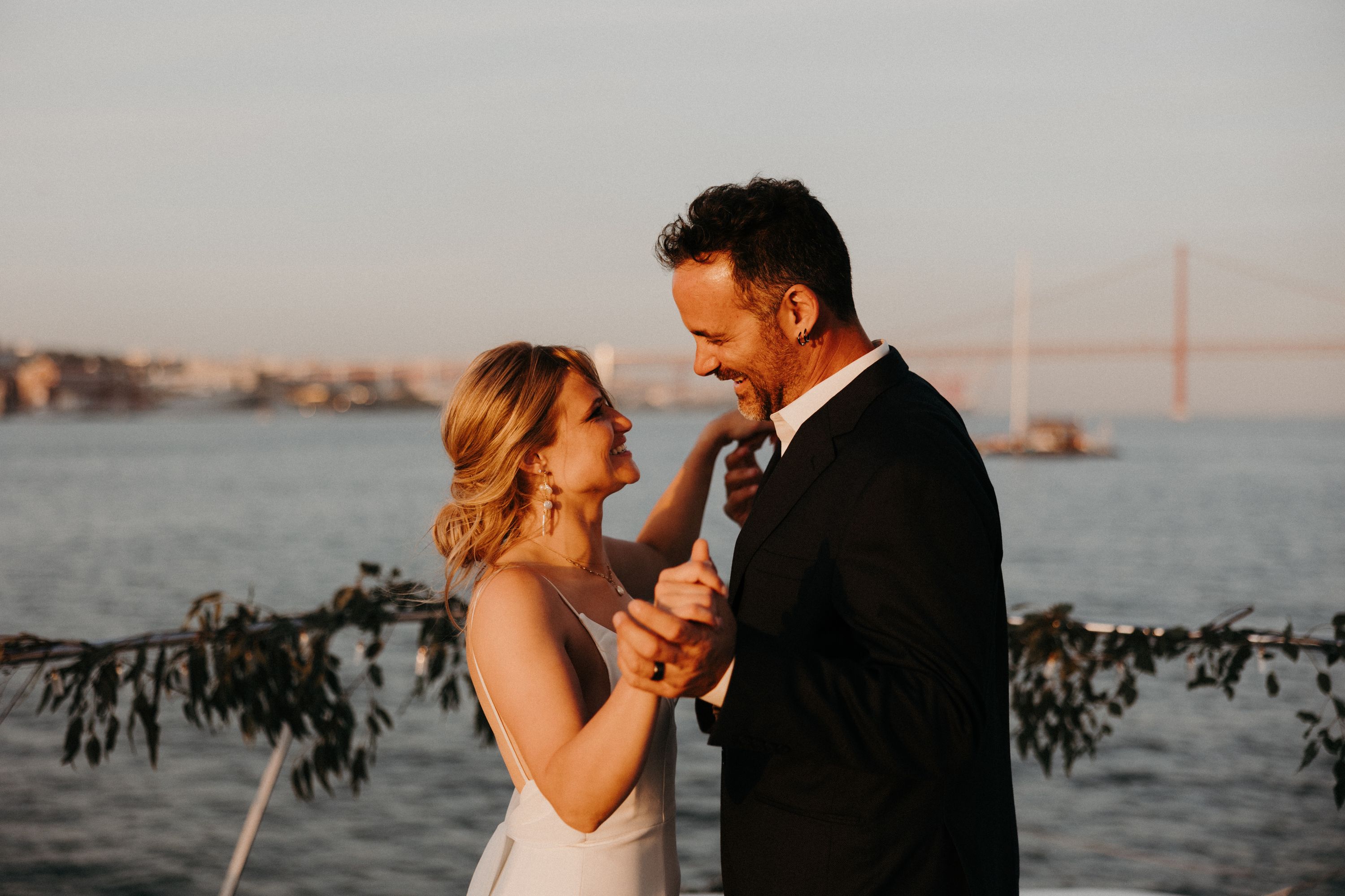 Bride and groom dance and smile with the Tagus River behind them during their destination wedding in Portugal