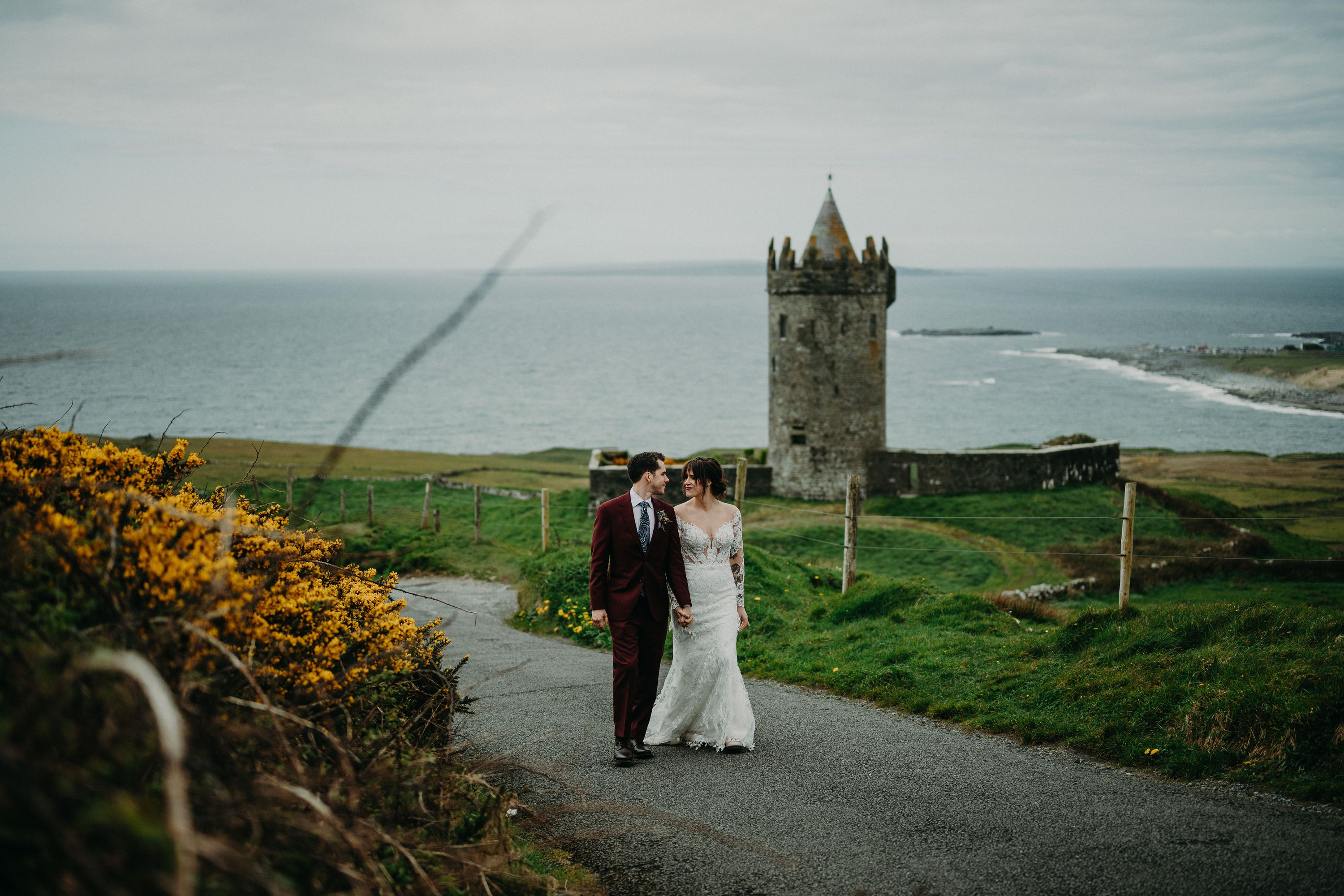 A bride and groom down a path with a dramatic tower behind them after their small wedding in Ireland