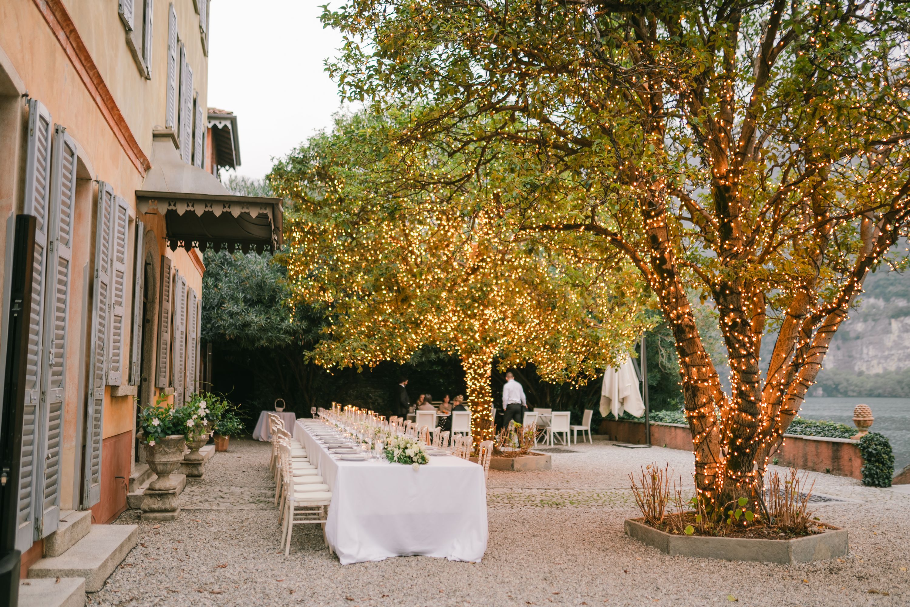 White long table with chairs arranged under the trees at a villa in Lake Como for the reception of a vow renewal in Italy
