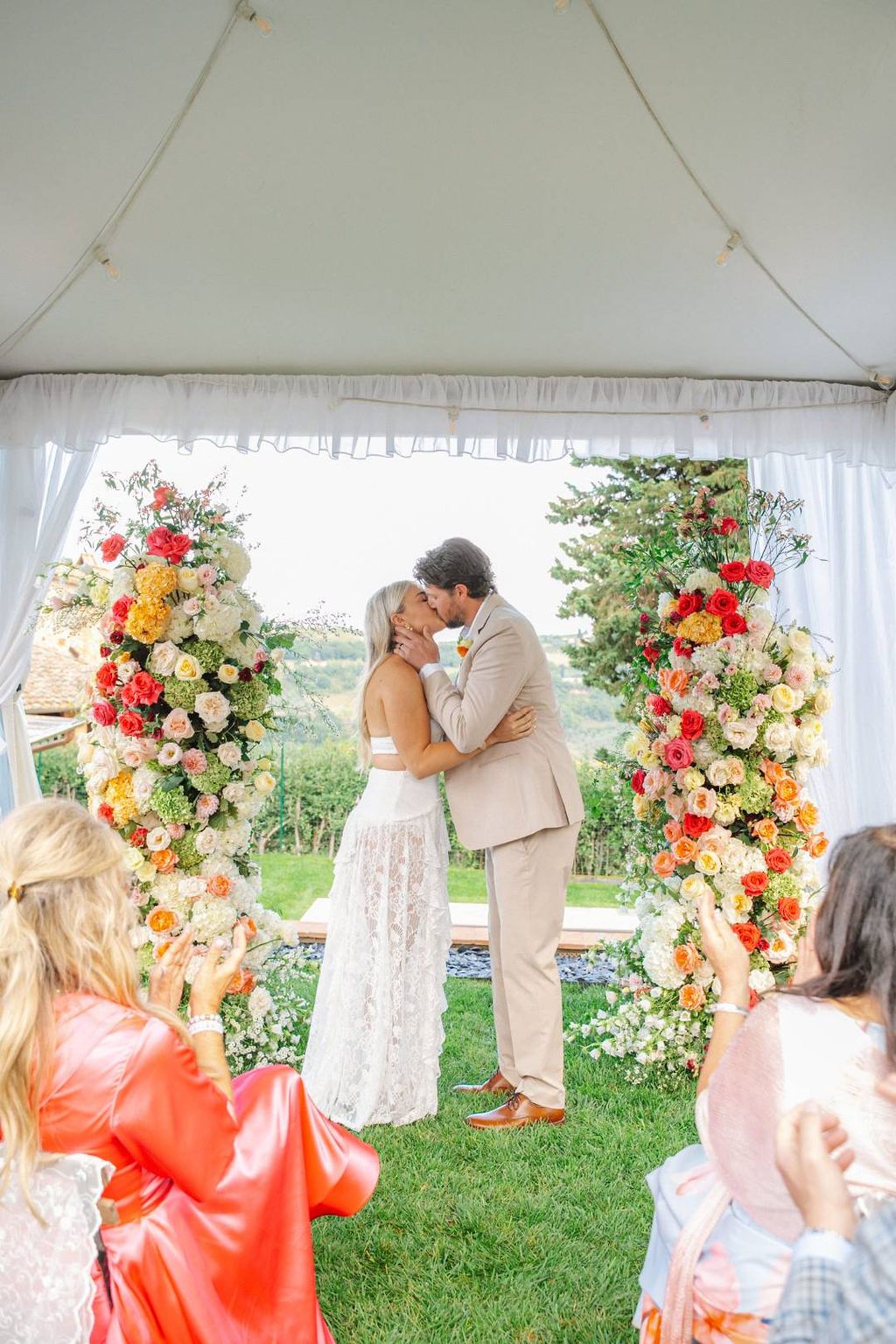 Bride and groom kiss under a white tent with vineyard views in the background during their small wedding in Italy