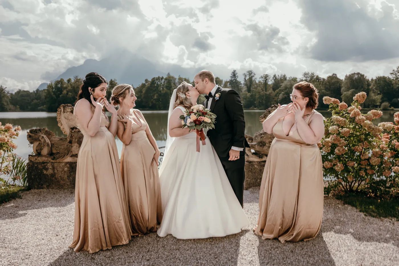 Newlyweds kissing as their small wedding party celebrates by the lake