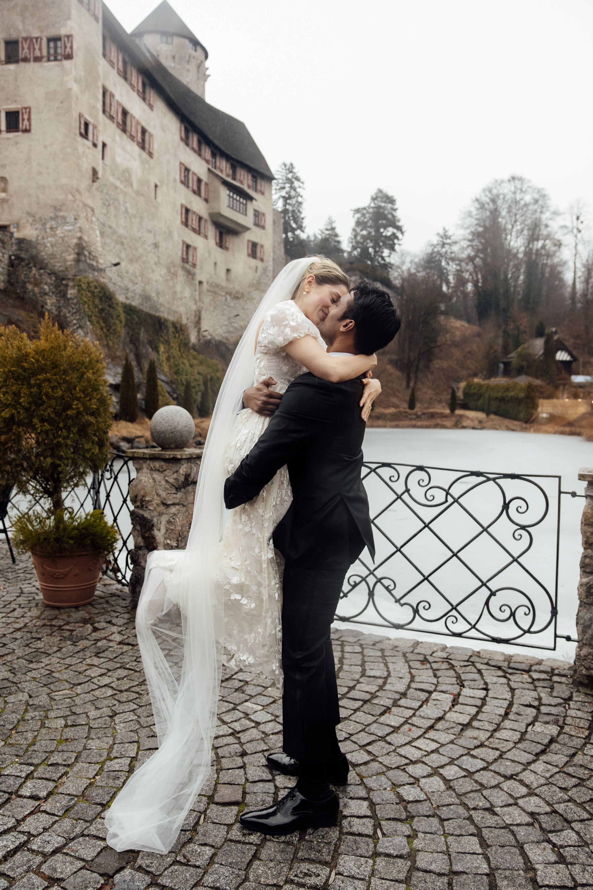 Groom lifts bride beside a castle lake during a romantic intimate wedding in Austria