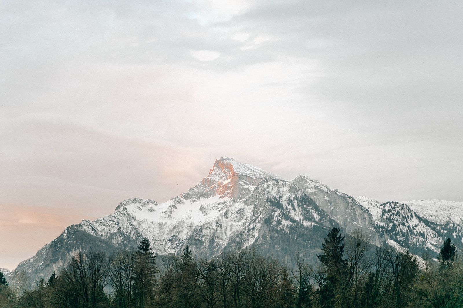 Snow-dusted mountain peak glowing at dusk above dark pines in Austria