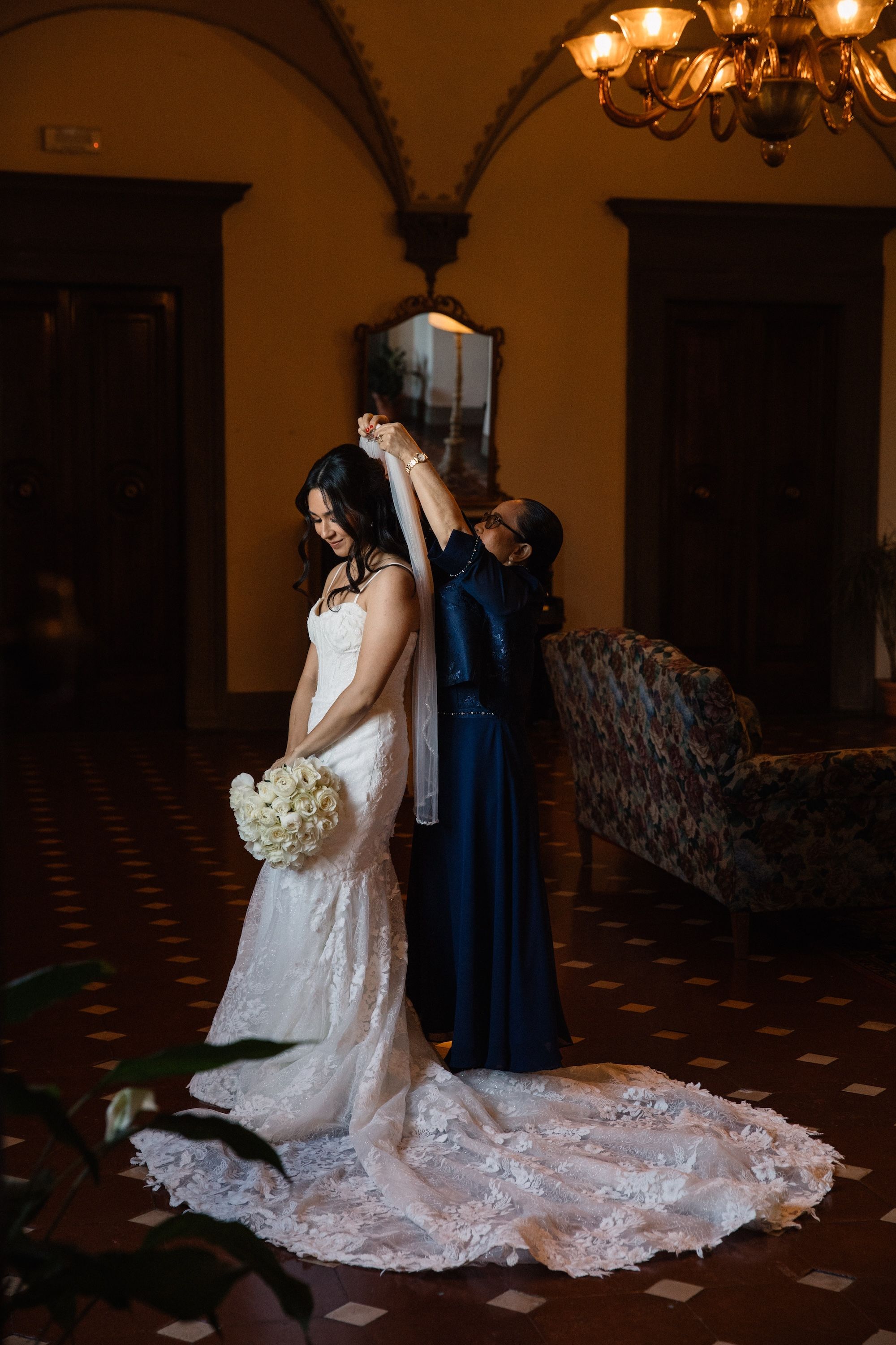 Mother of the bride helps her fix her veil while getting ready for the ceremony of her vow renewal in Italy