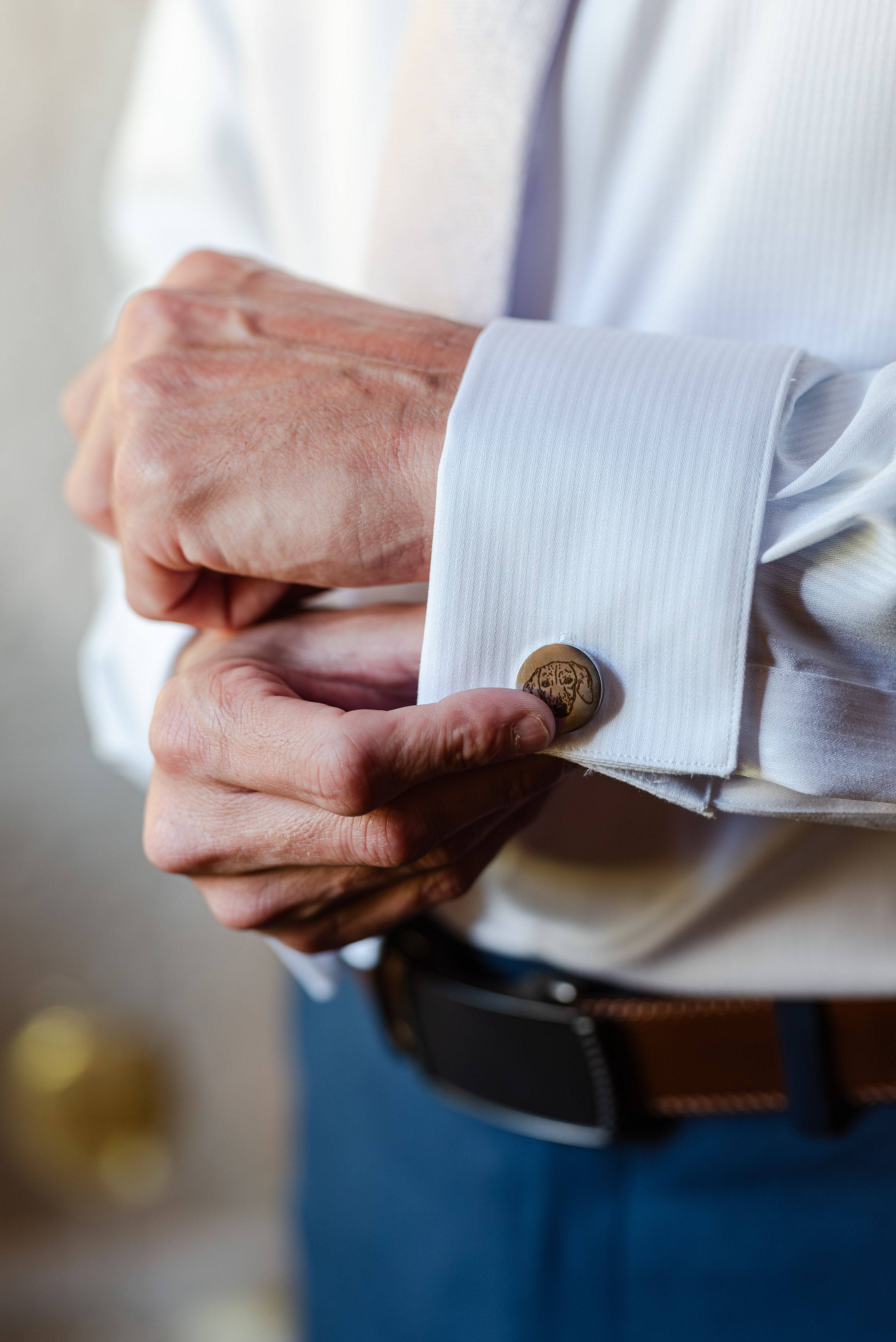 Groom fastening engraved cufflinks on a white shirt while getting ready for a small wedding in France