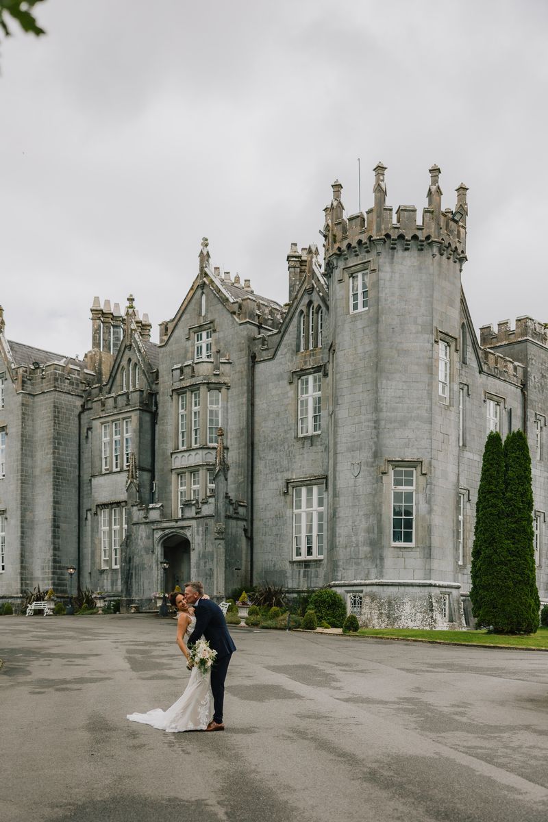 Groom kisses his bride during their destination wedding in Ireland, with a gothic castle in the background