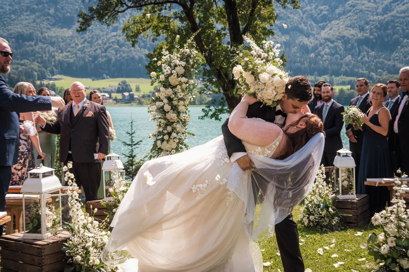 Newlyweds dip-kissing at a lakeside ceremony in Austria, guests all around