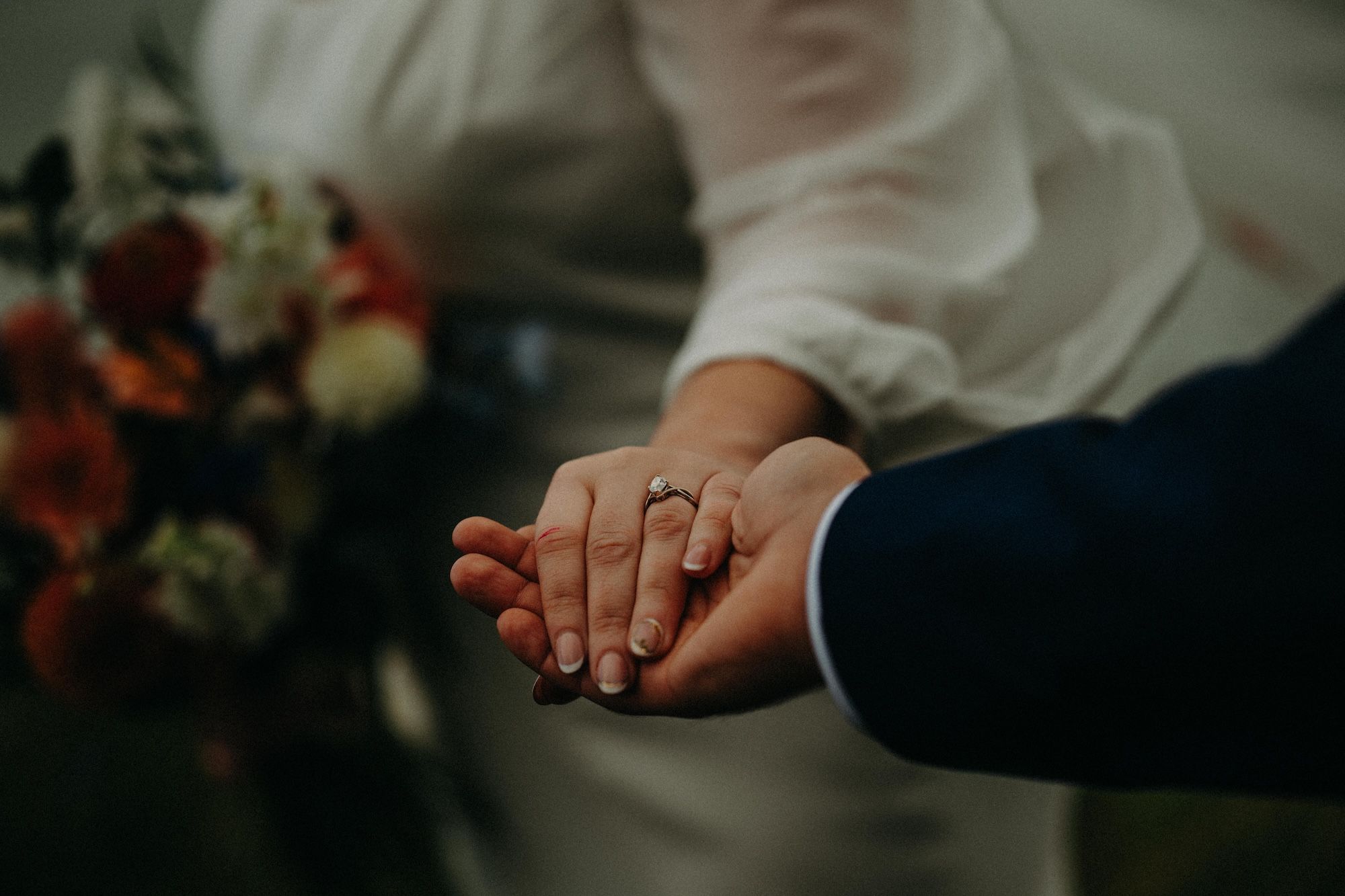 Two hands holding each other, one of them with a ring, in a gloomy and dramatic setting of their small wedding in Ireland.