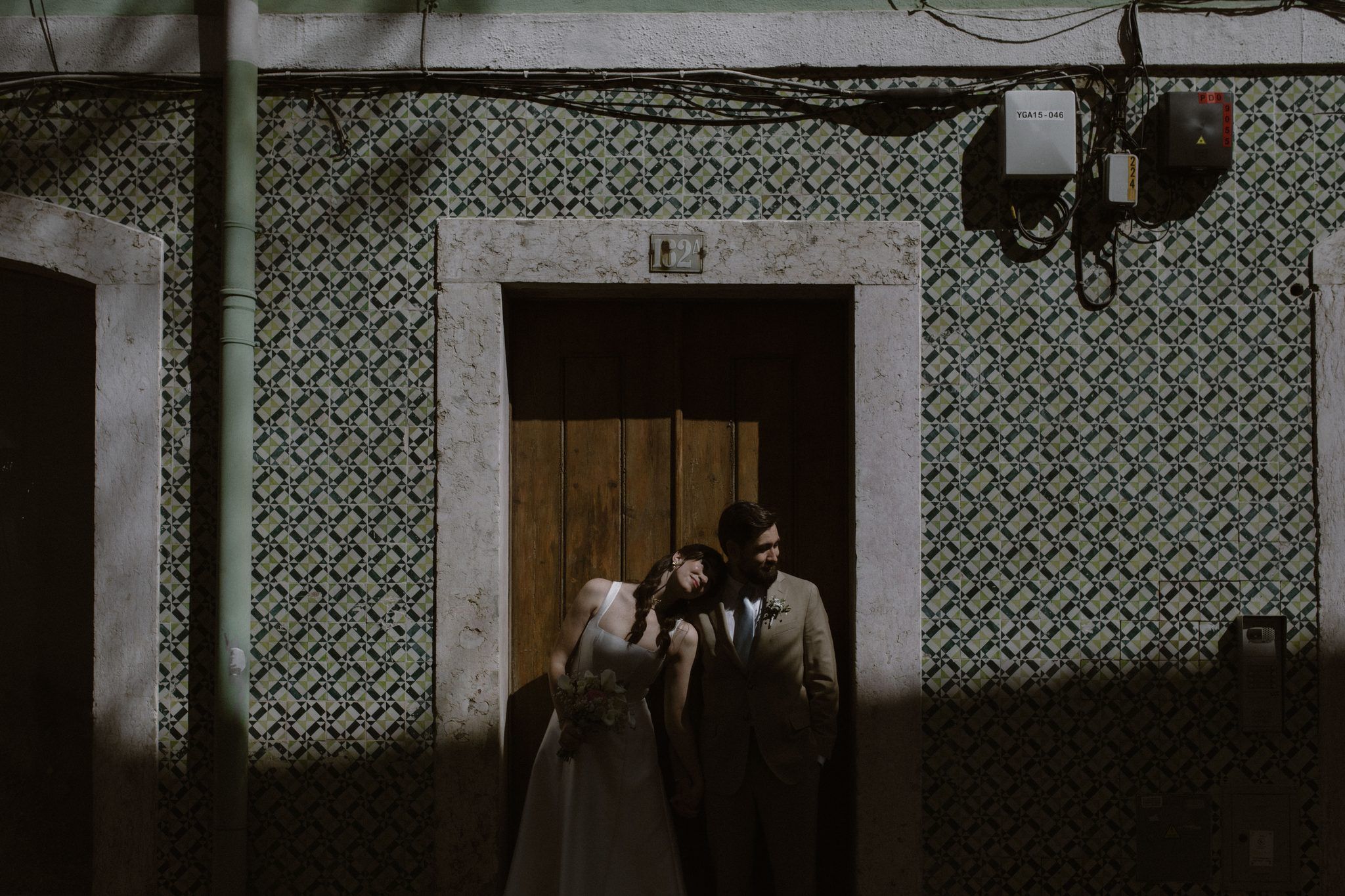 Bride leans into her groom outside a blue-and-white azulejo-tiled townhouse during their Portugal elopement, bouquet in hand.