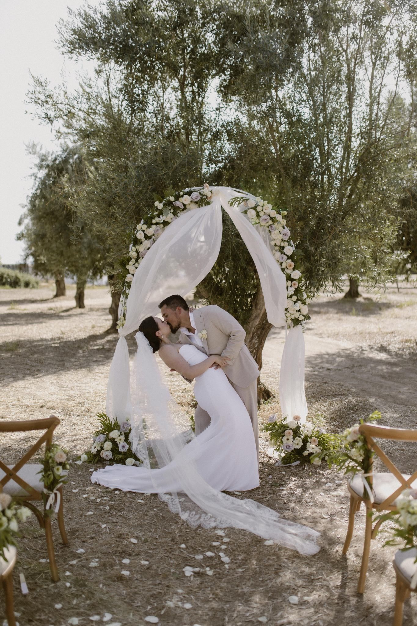 Bride and groom kiss under a simple floral and cloth wedding arch during their outdoor micro wedding in Portugal