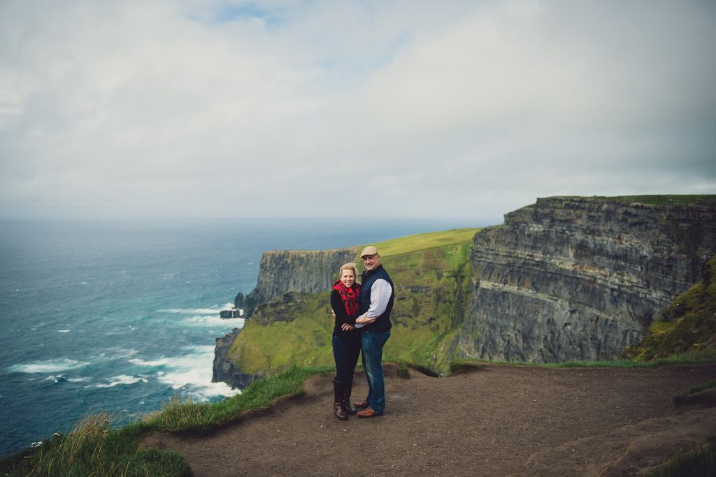 Man and woman in casual clothing at the top of the Cliffs of Moher on a bright day