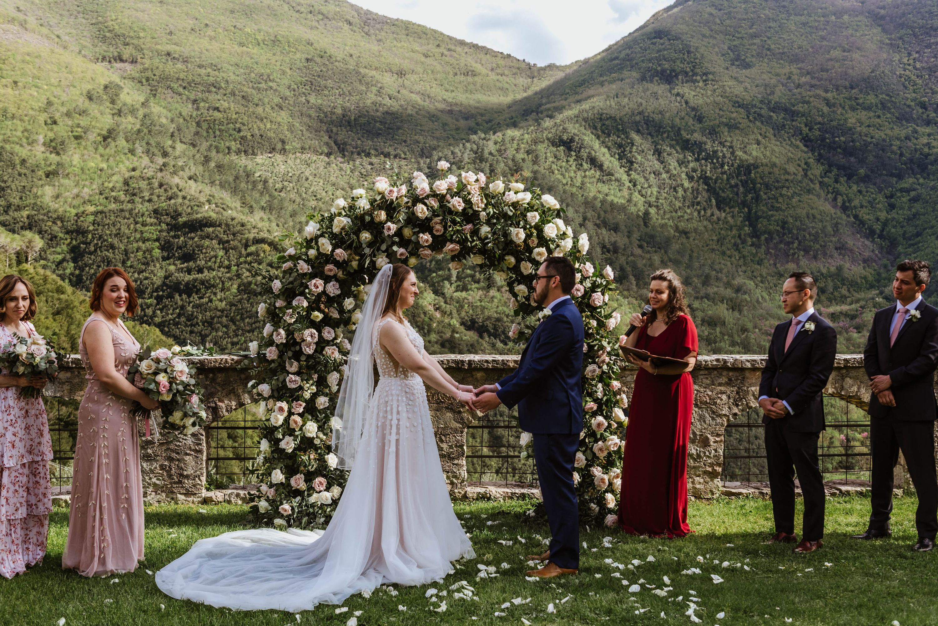 Couple holding hands during their ceremony for a destination wedding in Italy with mountains in the background.