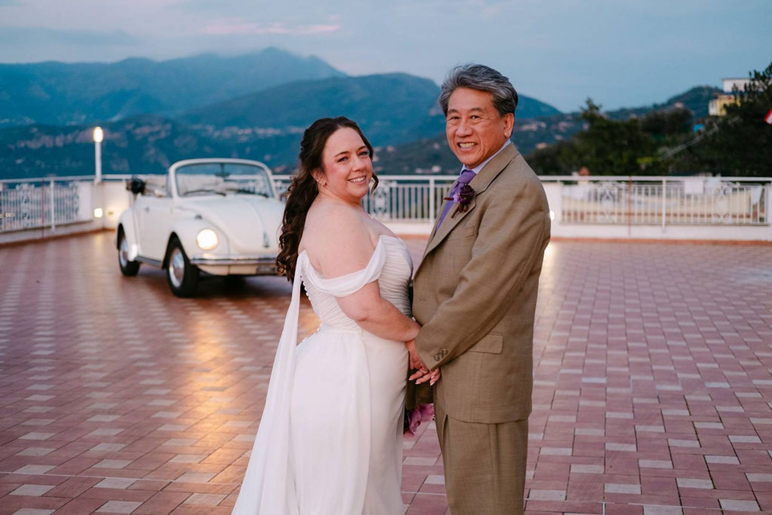 Newlyweds pose together at dusk with a vintage car after an intimate wedding in Italy