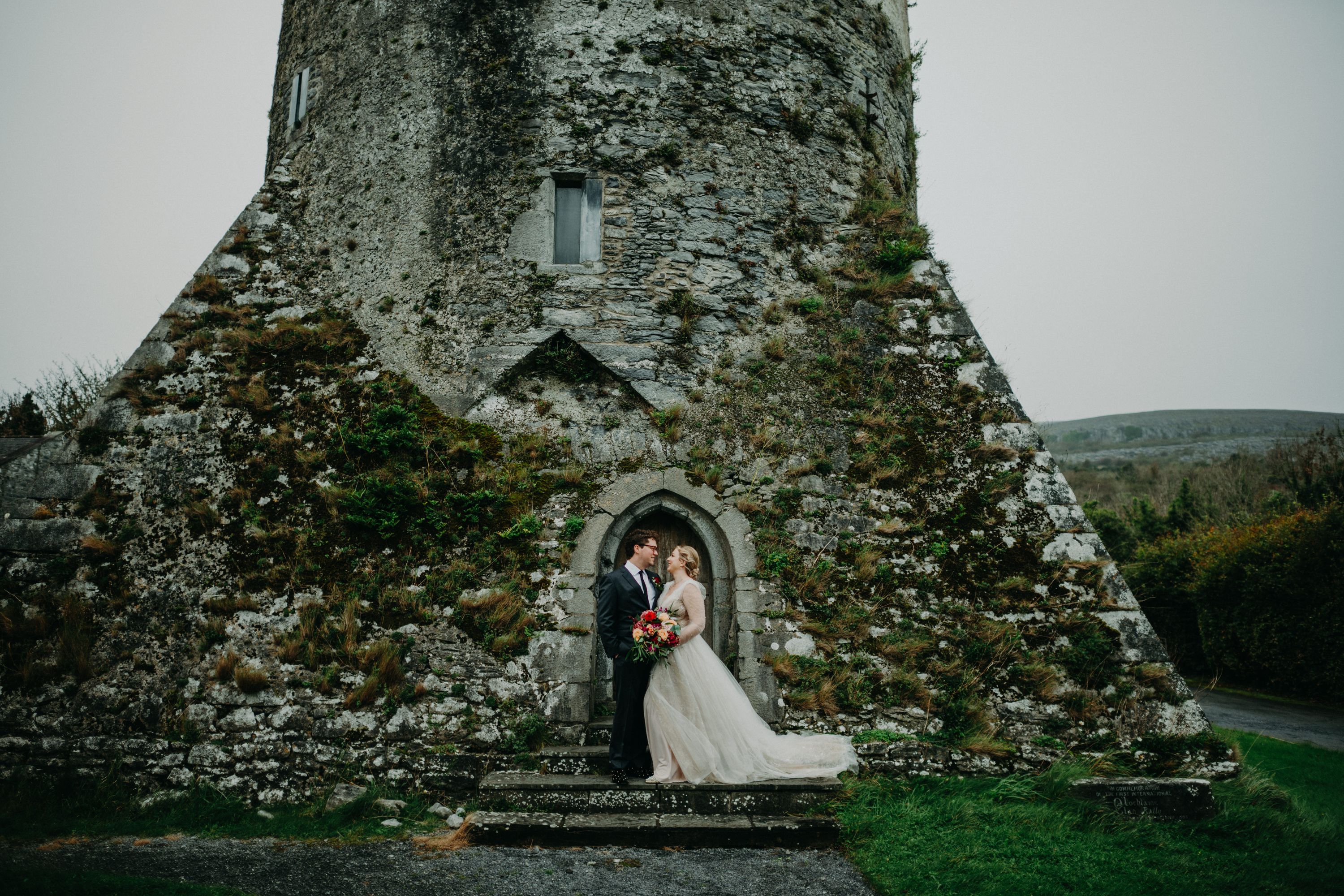 Bride and groom share a moment outside a medieval tower during an intimate wedding in Ireland