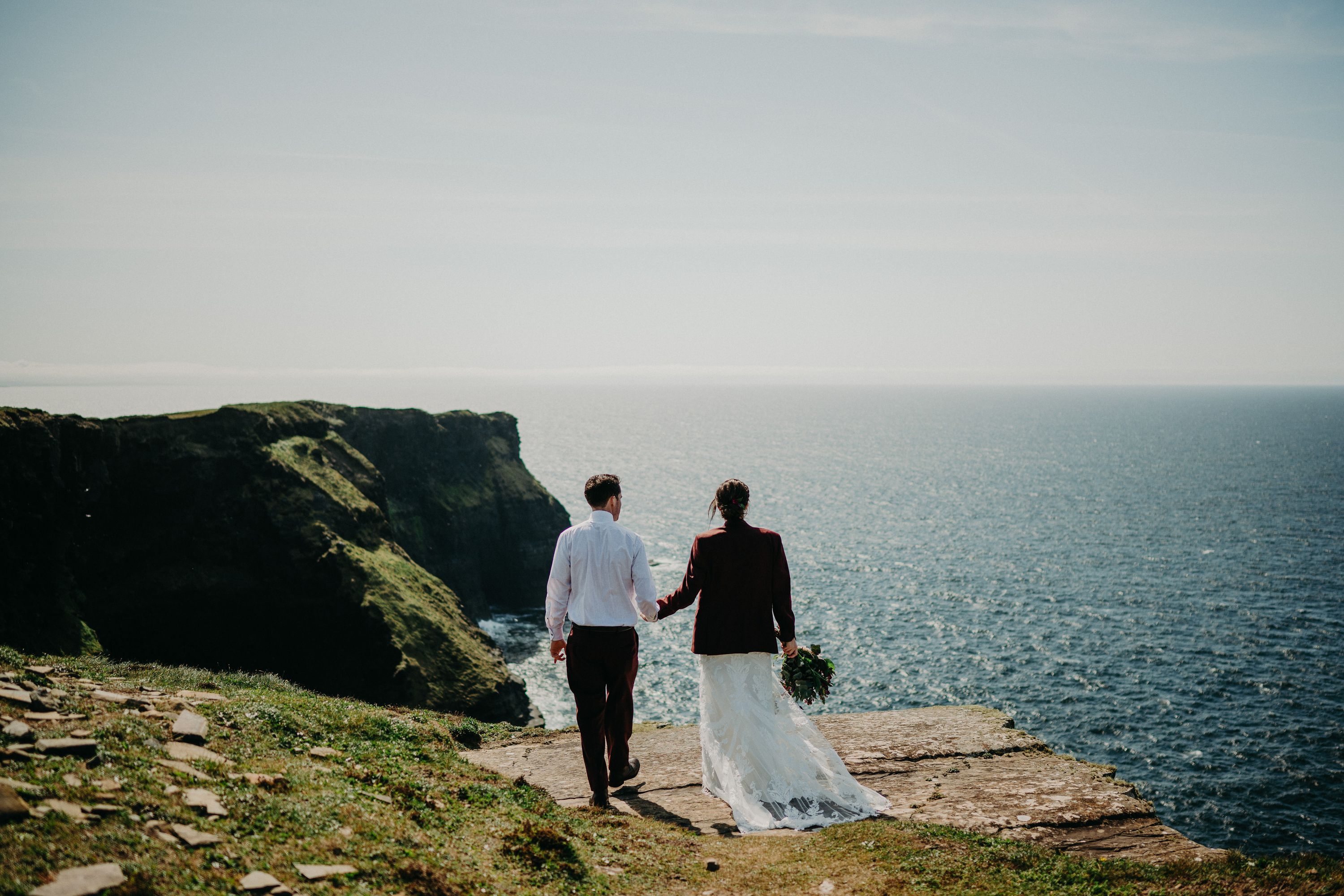 A bride and groom look at the ocean before them while they stand on top of a cliff during their small wedding in Ireland