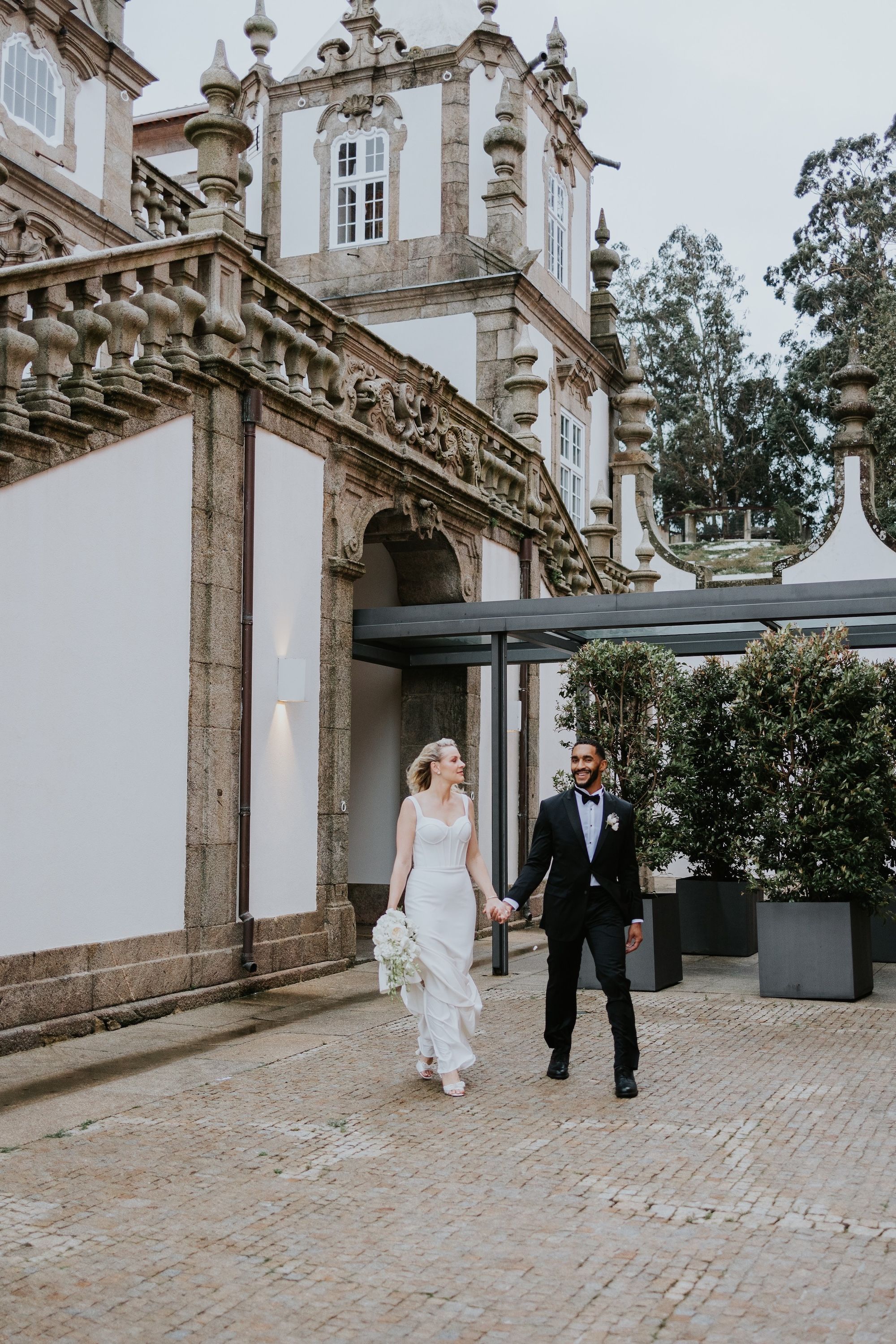Newlyweds hold hands while walking outside the palace hotel where they got married in Portugal