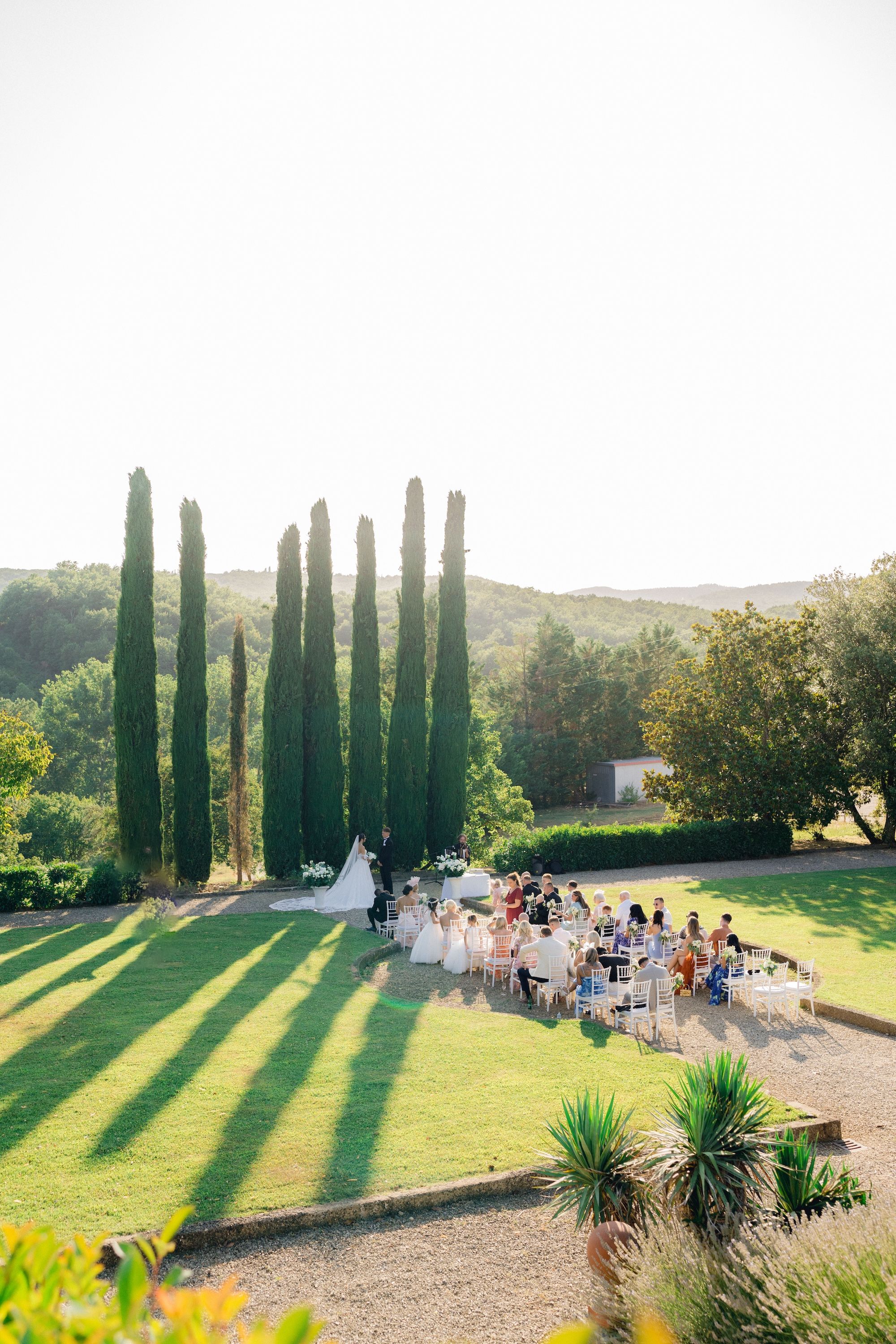 An outdoor ceremony of a destination wedding in Tuscany with a small group of guests overlooking forested hills.