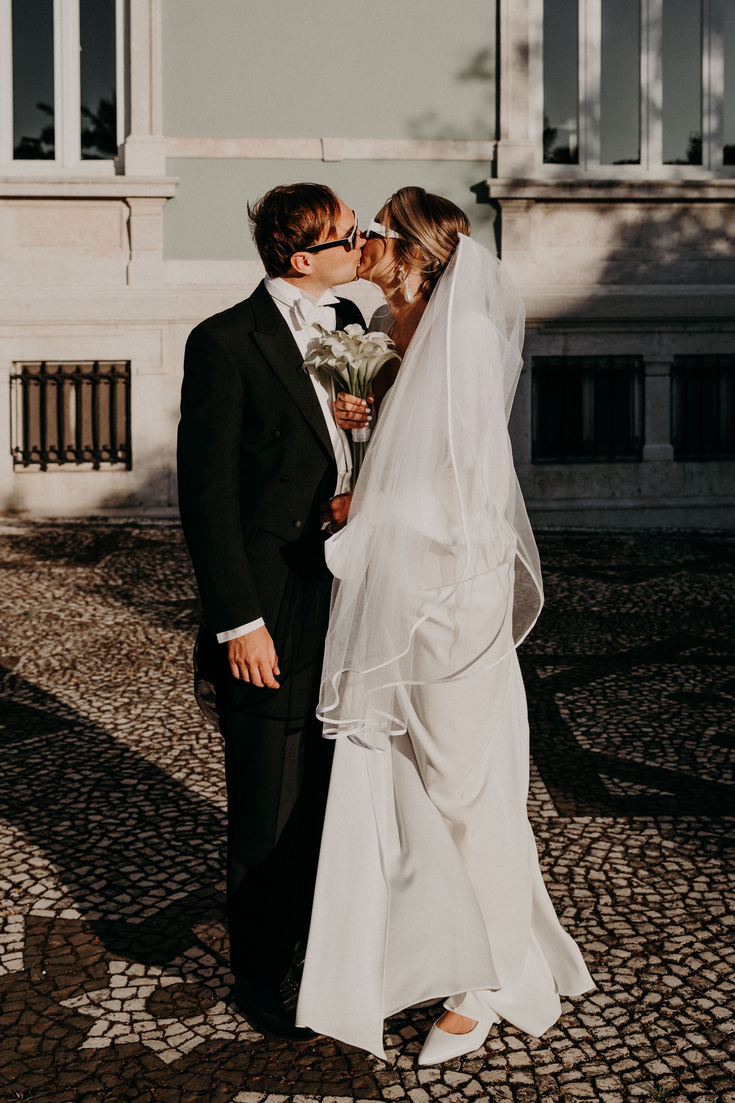 Bride and groom kissing outdoors in front of a palace during their destination wedding in Portugal
