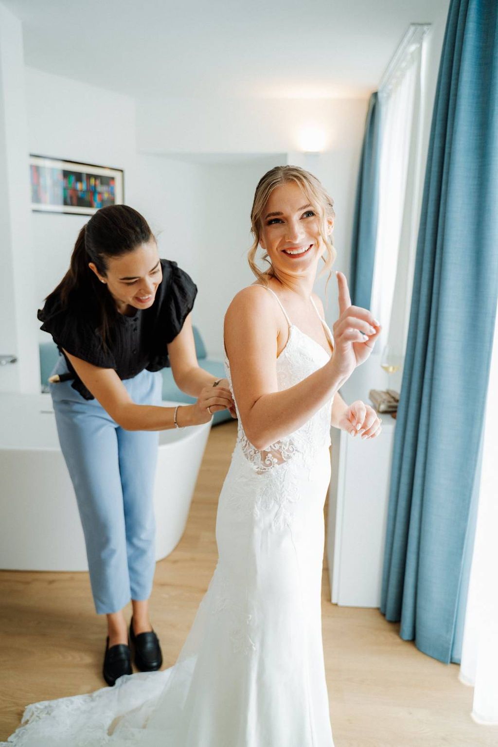 Bride happily pointing up as her elopement planner in Italy fixes the back of her wedding dress