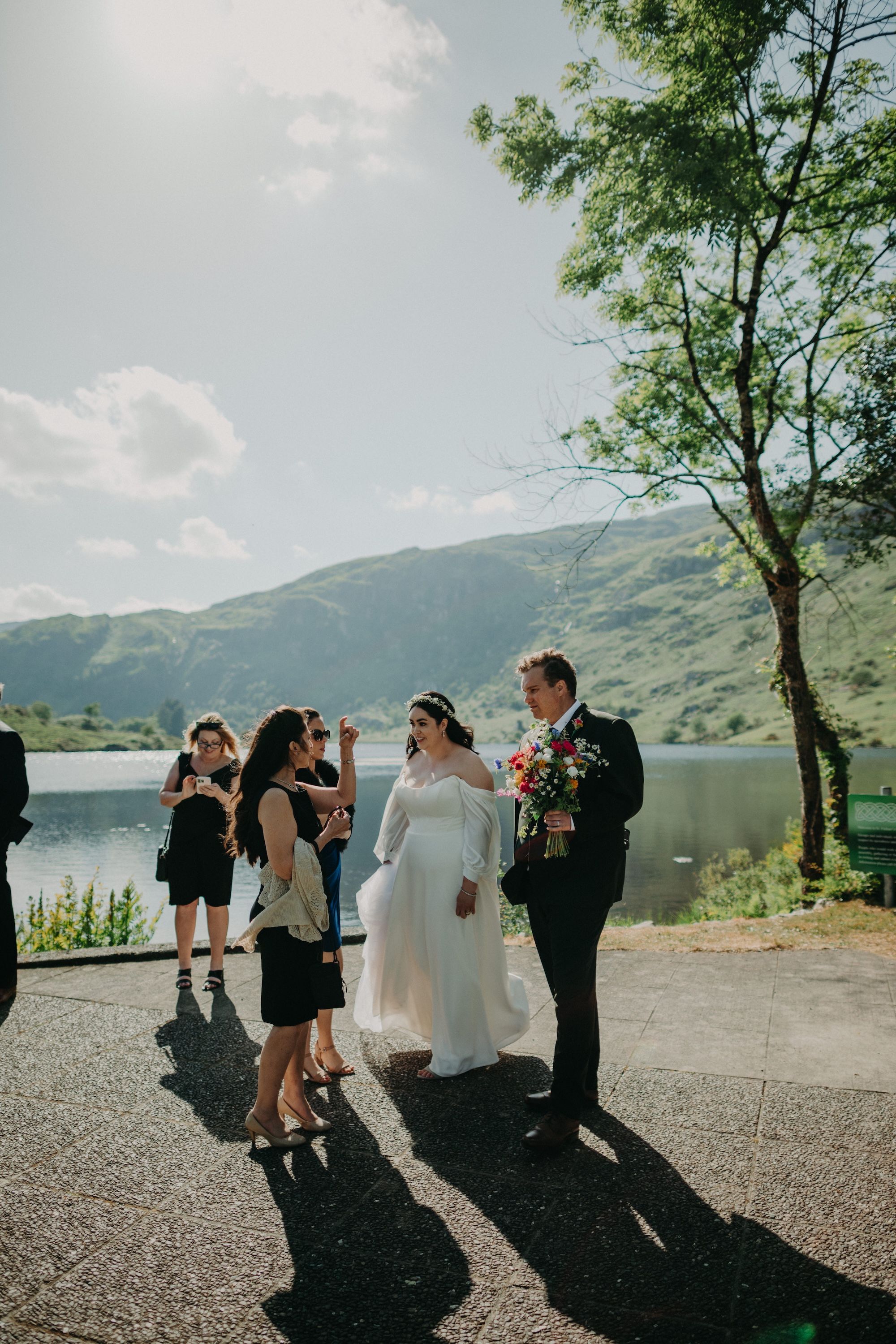 Bride and groom talk to guests outdoors with lake and mountains in the background during their micro wedding in Ireland
