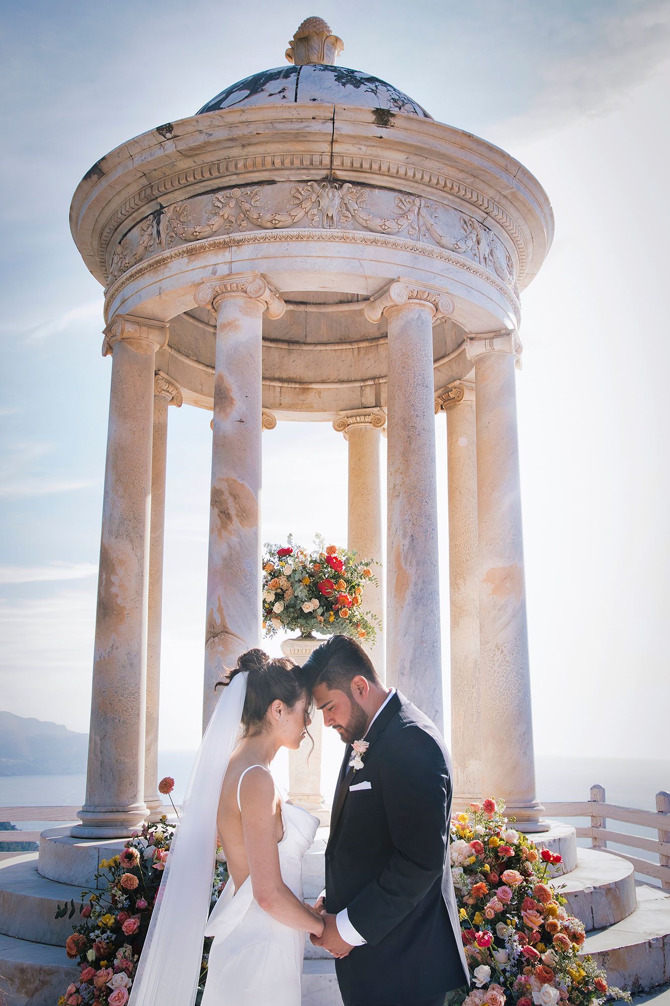Bride and groom with heads together and a white stone gazebo in the background during their destination wedding in Spain