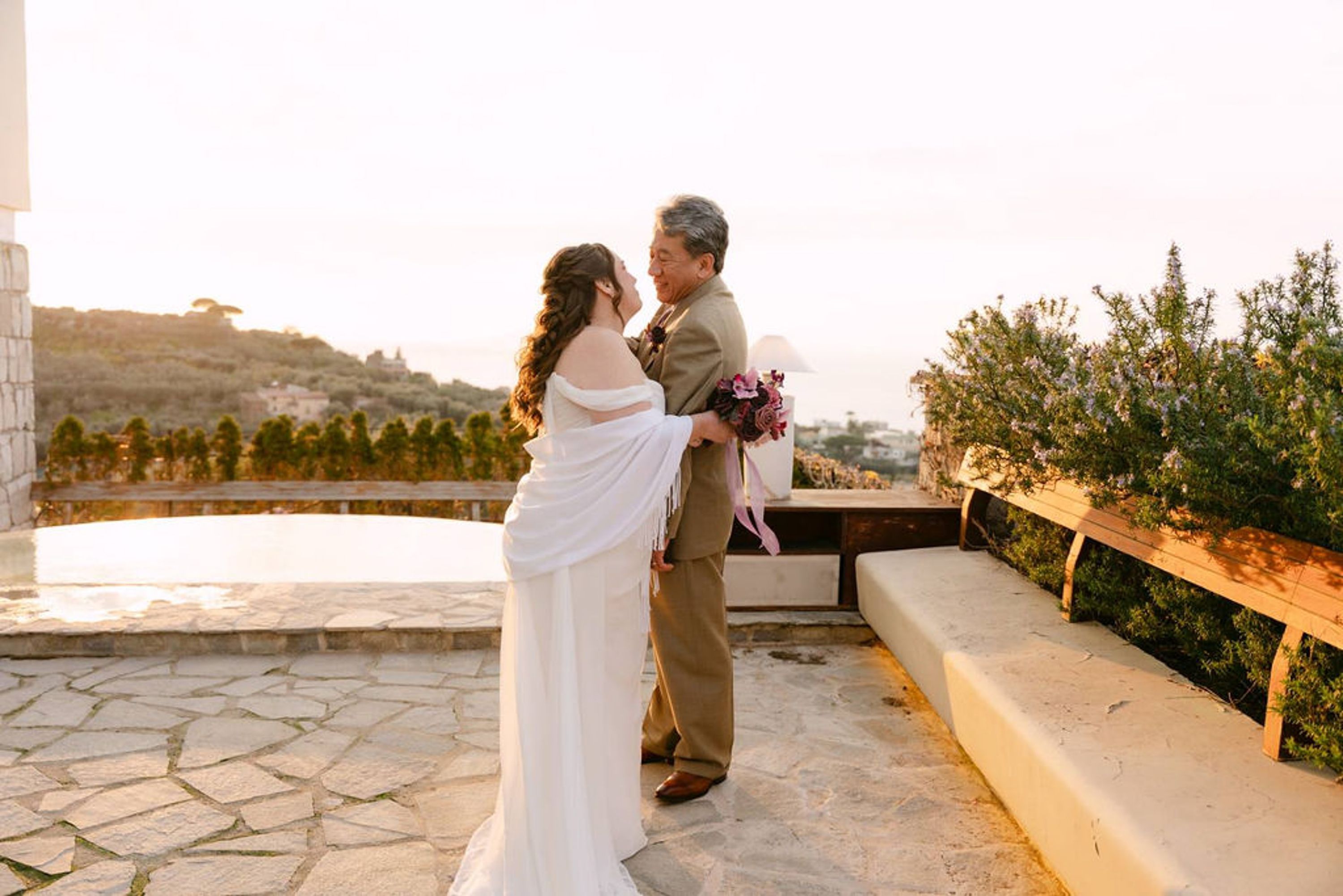 Bride and groom embracing on a sunlit terrace overlooking the coast in Italy
