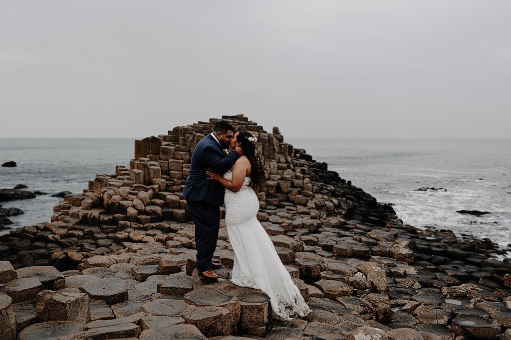 Newlyweds having a photoshoot in the Giant’s Causeway with rows of basalt columns and the ocean at the back