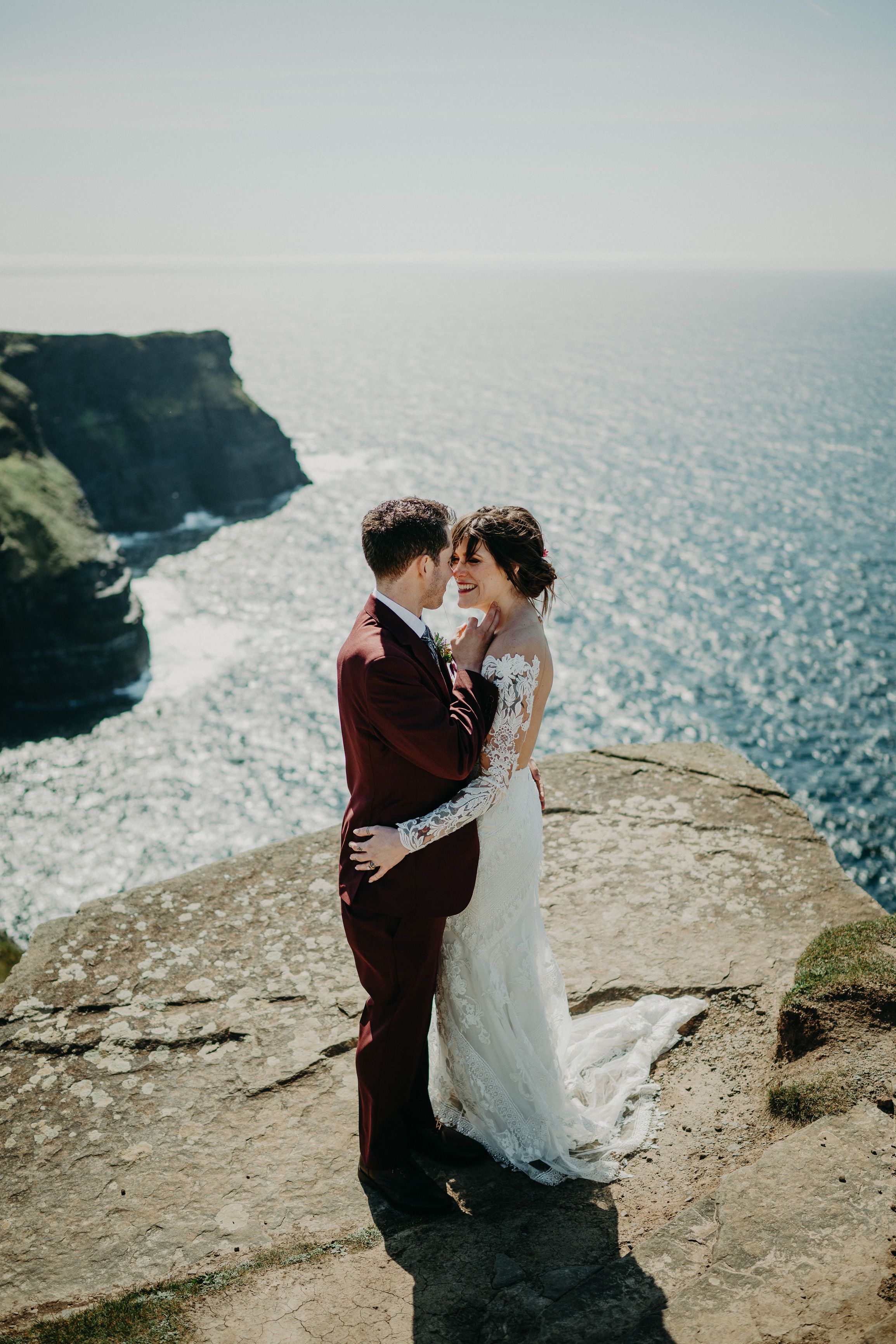 A bride and groom having their portait taken on top of a cliff with a captivating view of the sea behind them