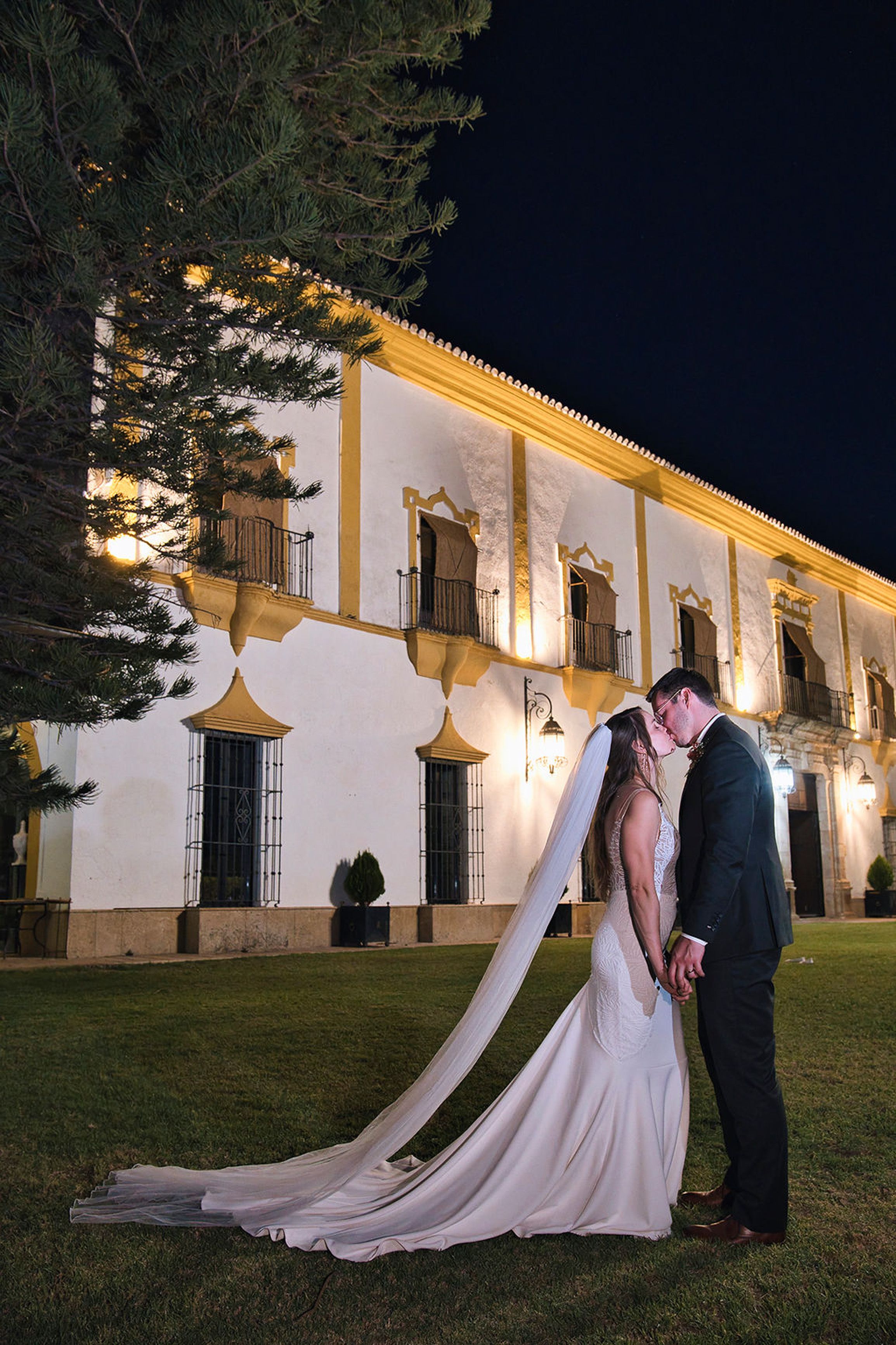 Bride and groom sharing a kiss outside a beautifully lit manor after an intimate wedding in Europe