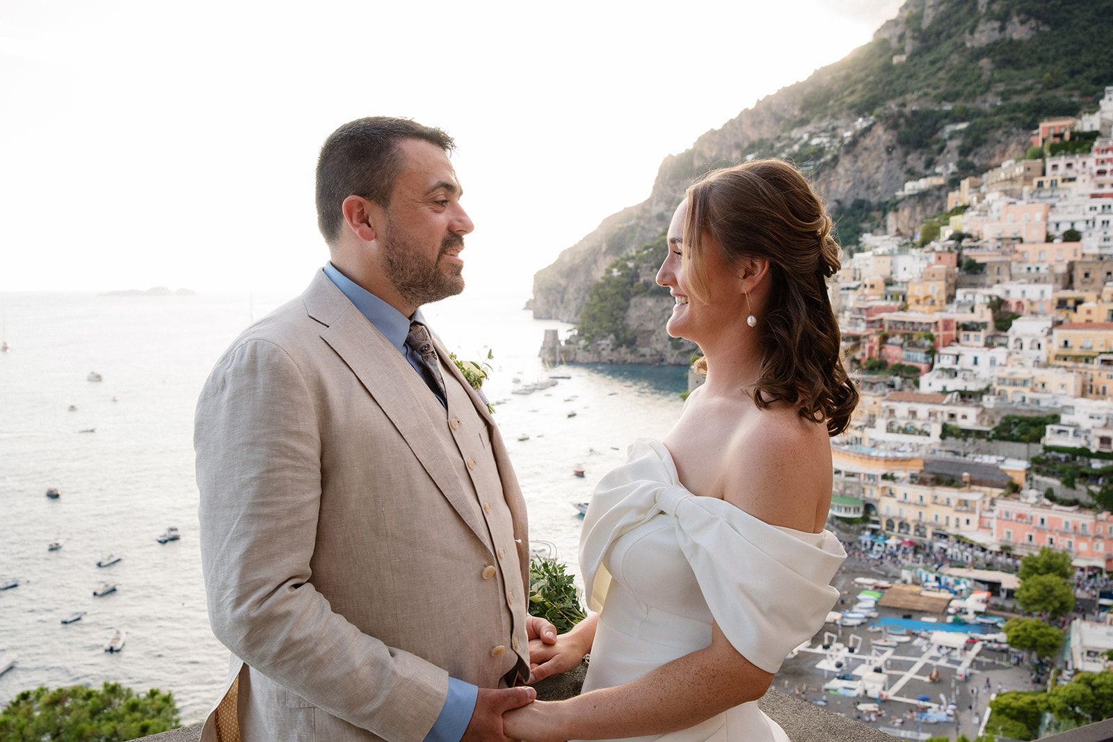Bride and groom holding hands atop a terrace with Amalfi Coast in the background