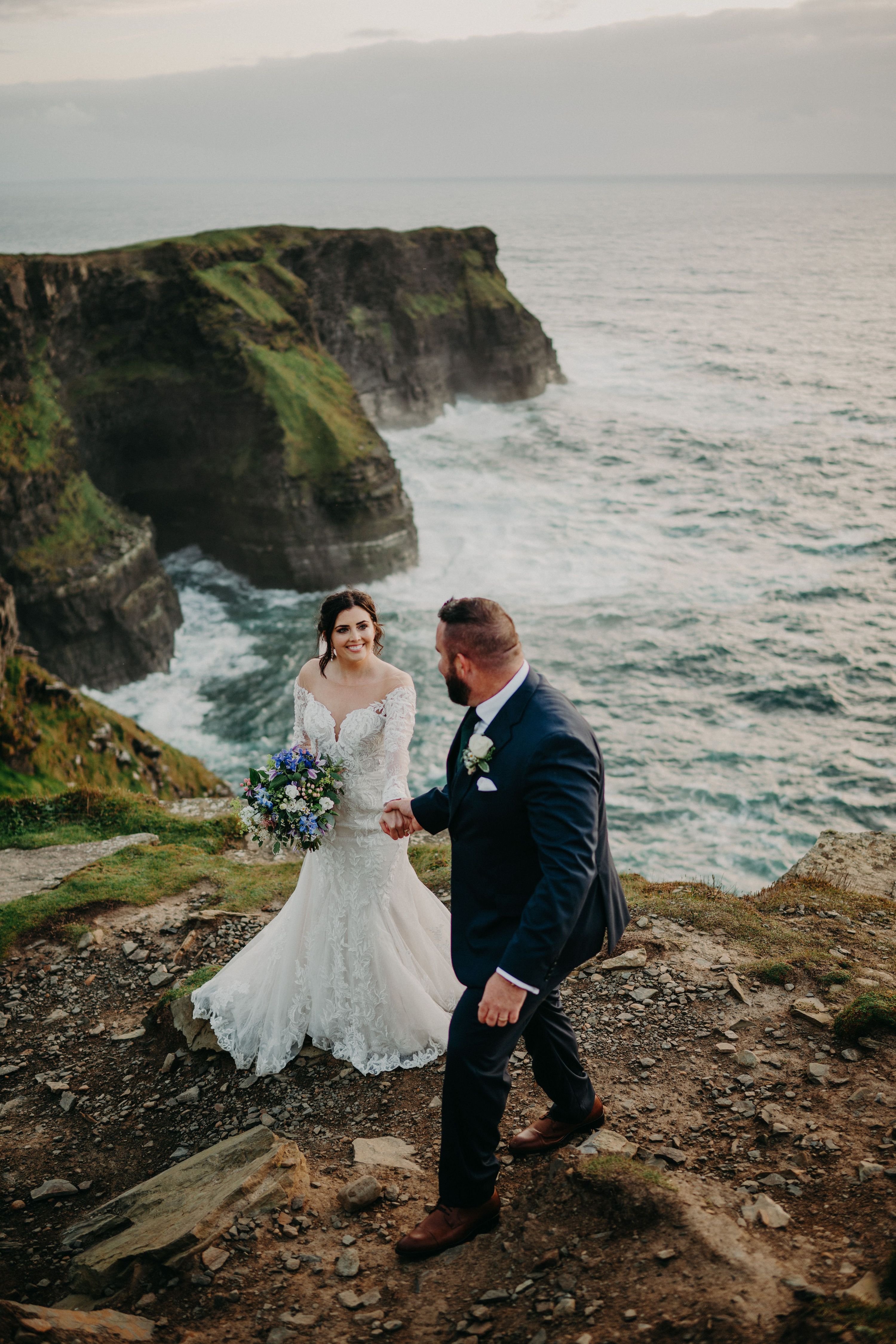 Bride and groom looking at each other during their photoshoot atop Hag’s Head with cliffs and the ocean in the background