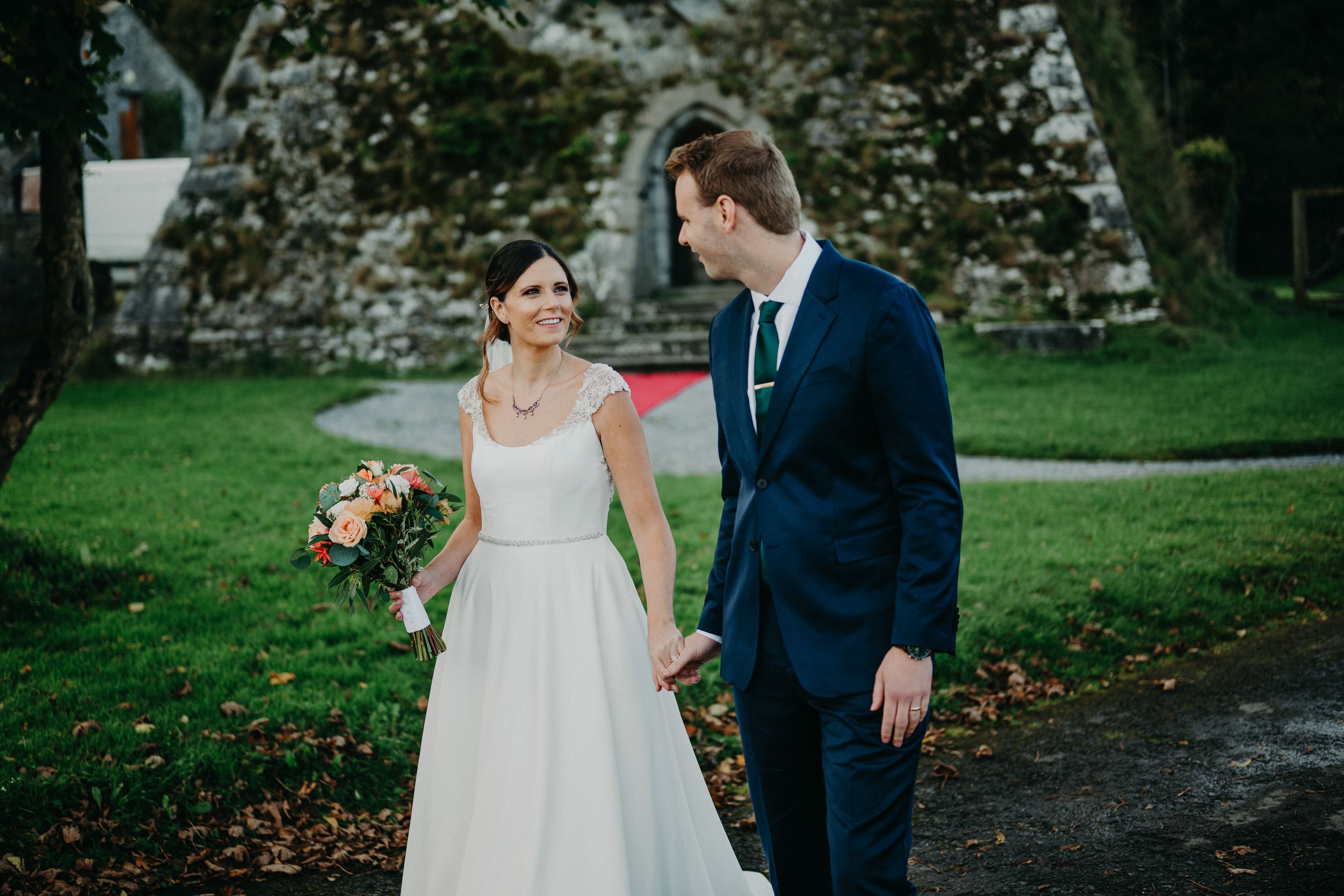 Newlyweds walking hand in hand through castle grounds after a small wedding in Ireland.