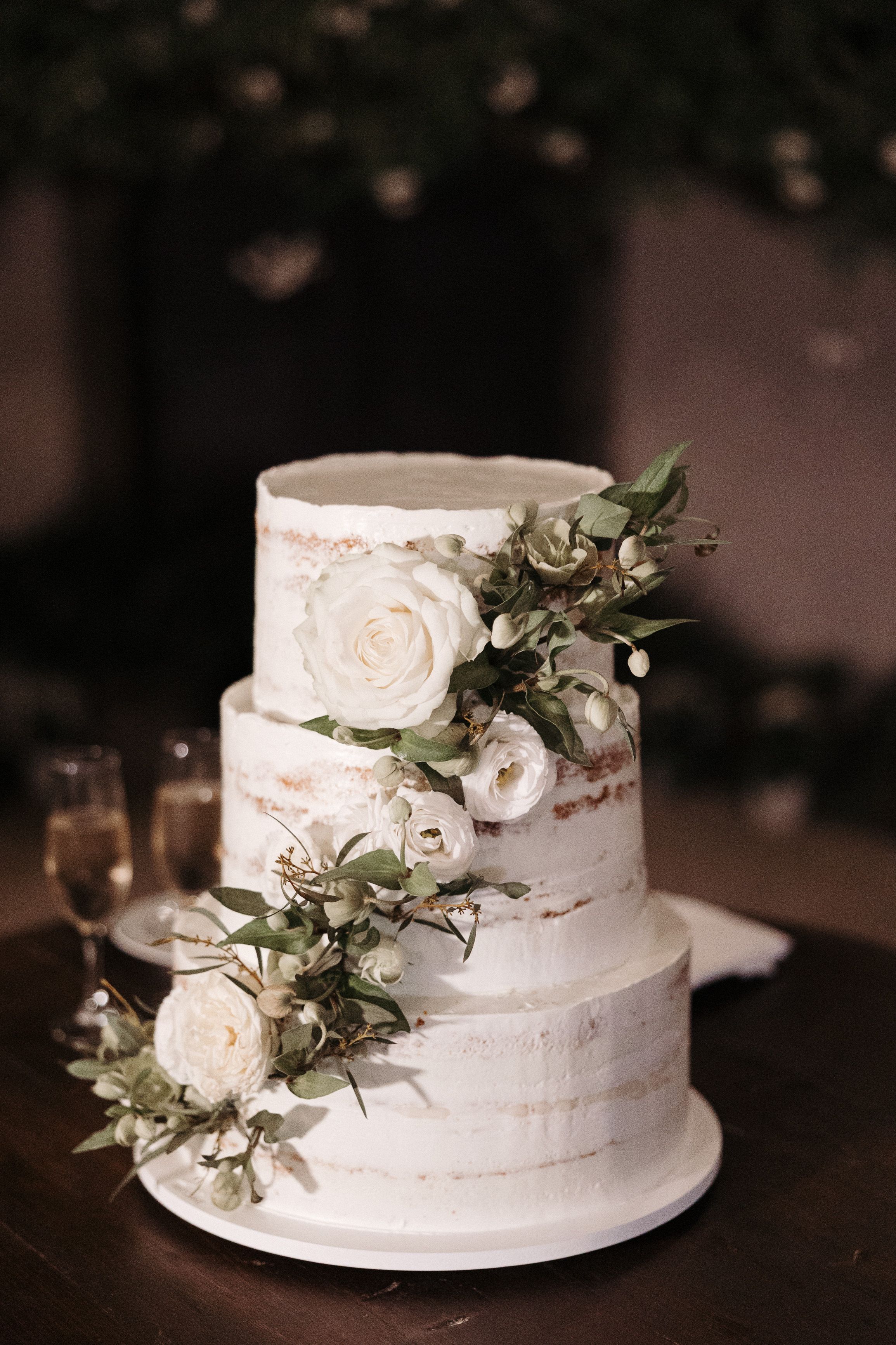 Three-tier wedding cake adorned with white roses and greenery at an intimate wedding in Portugal