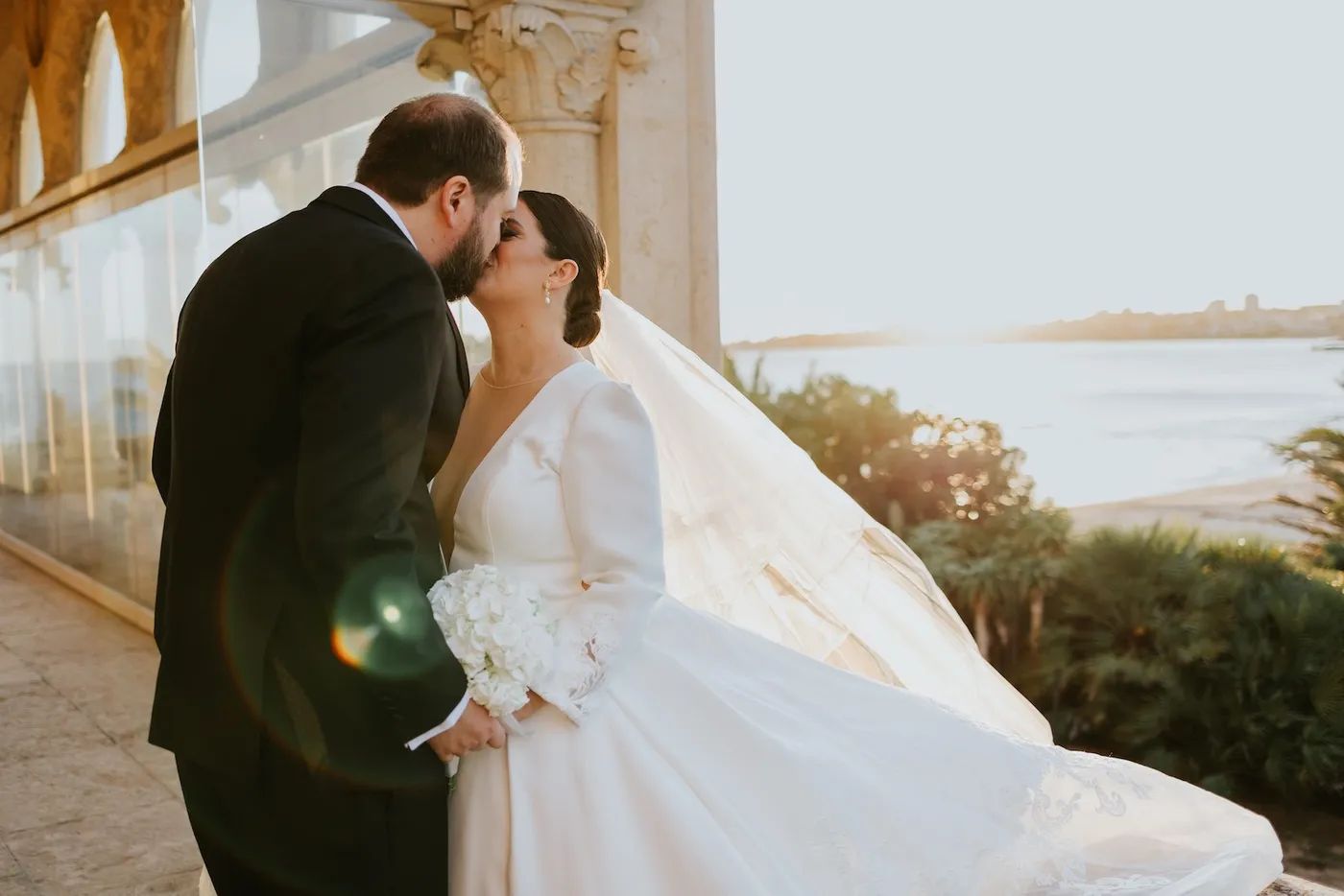 Groom kissing his bride at a balcony of a historic castle overlooking the ocean