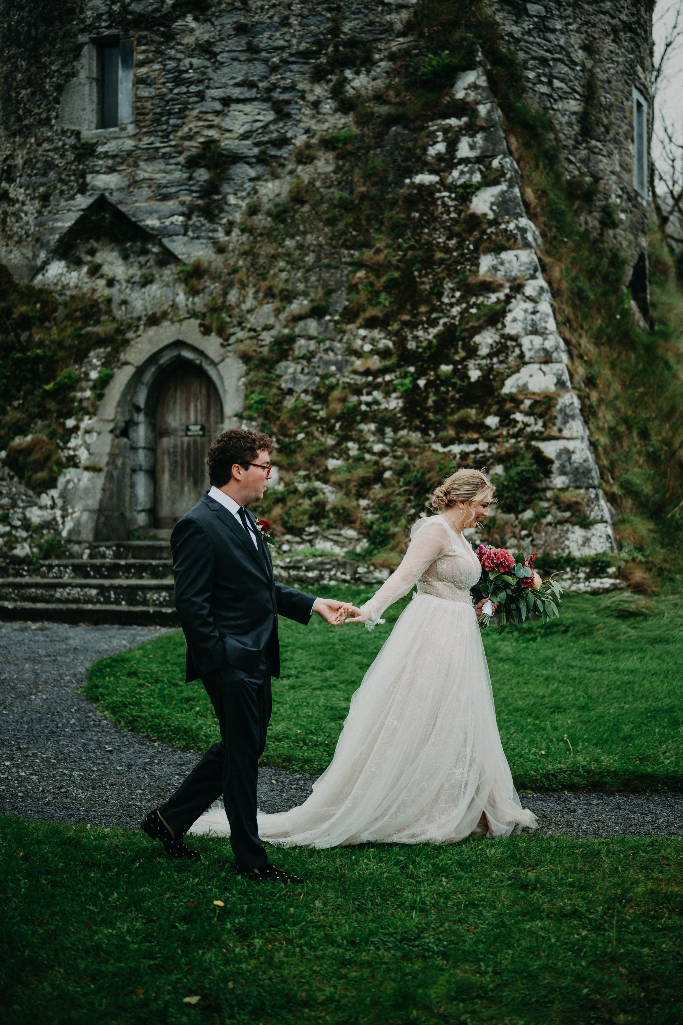 Bride leads groom across castle grounds during an intimate wedding in Ireland beside a medieval tower