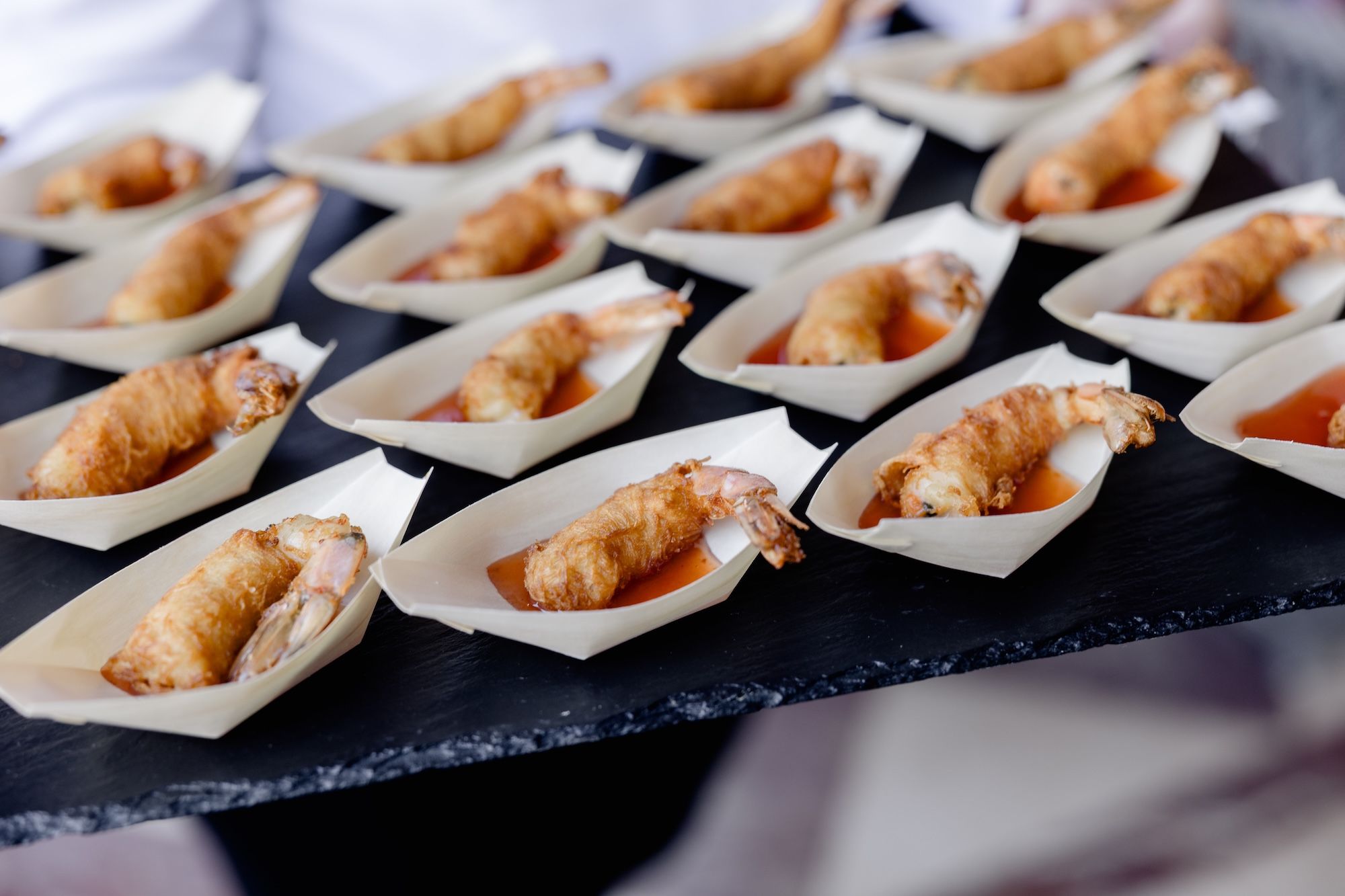 16 bowls of fried shrimp dish in sauce on a tray