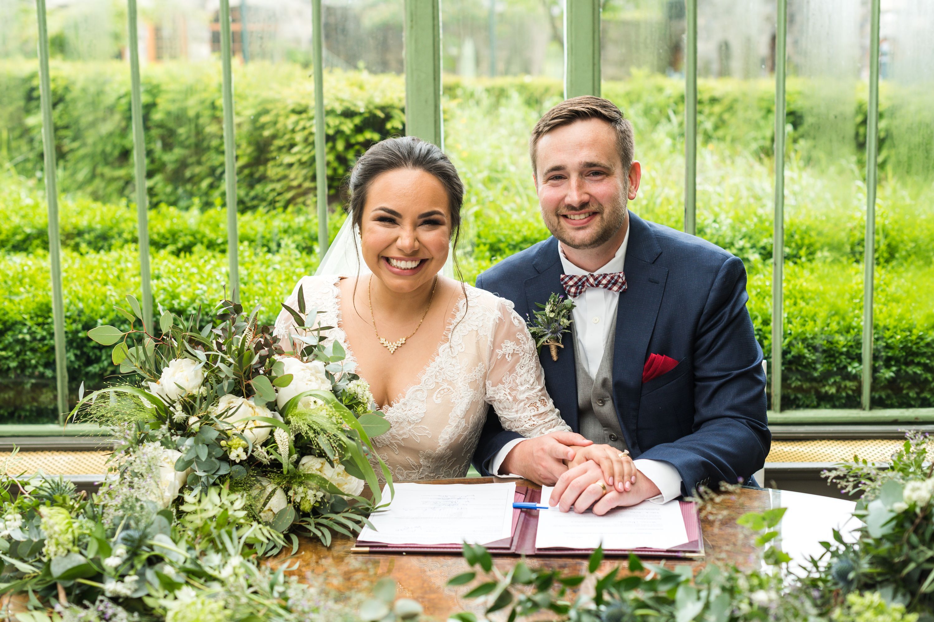 Bride and groom smile at the camera while they are holding a pen and a paper