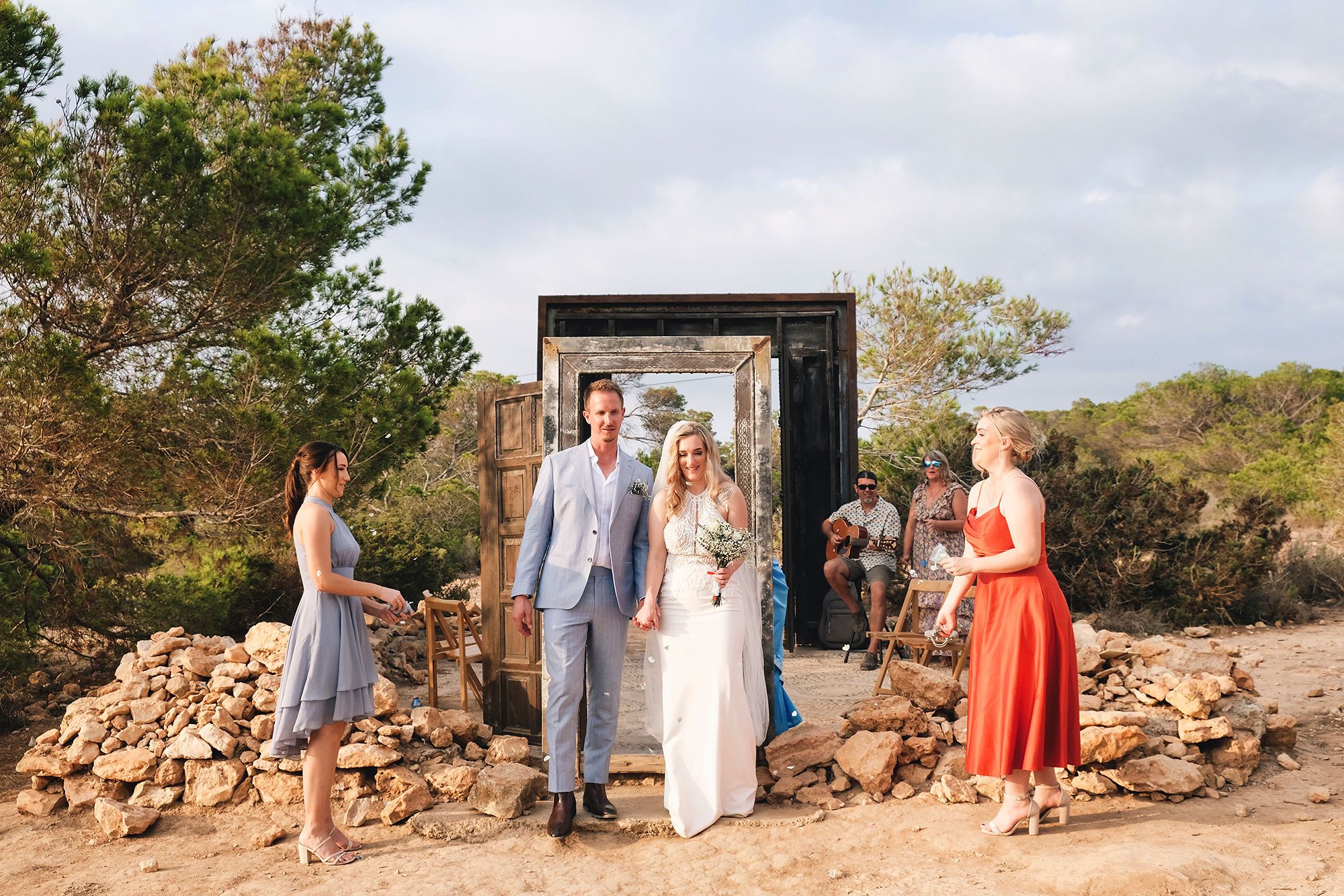 Newlyweds walk after ceremony with two guests standing in a beach wedding in Spain