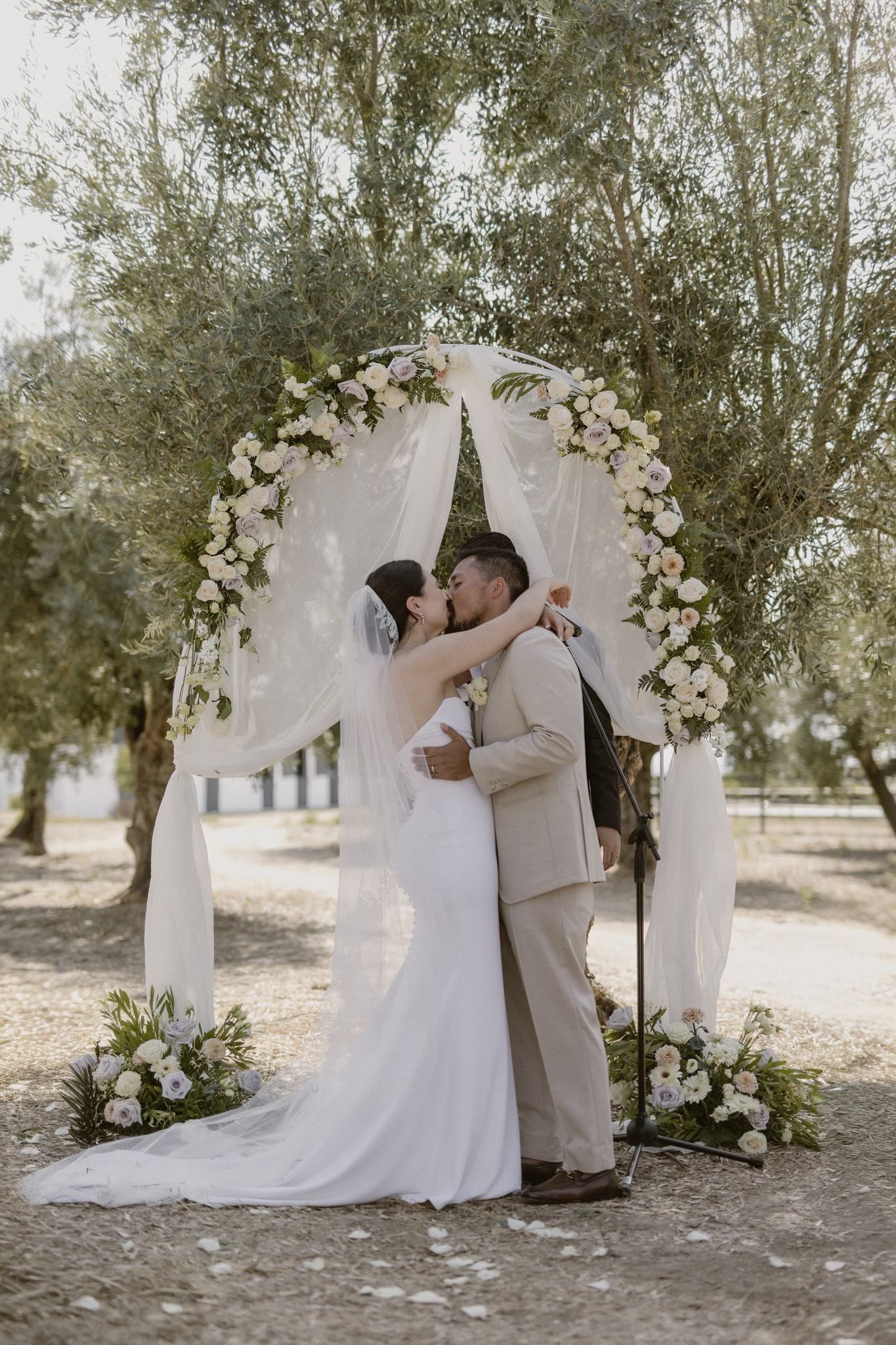 Bride and groom kisses in the middle of a simple floral and cloth wedding arch during a micro wedding in Portugal
