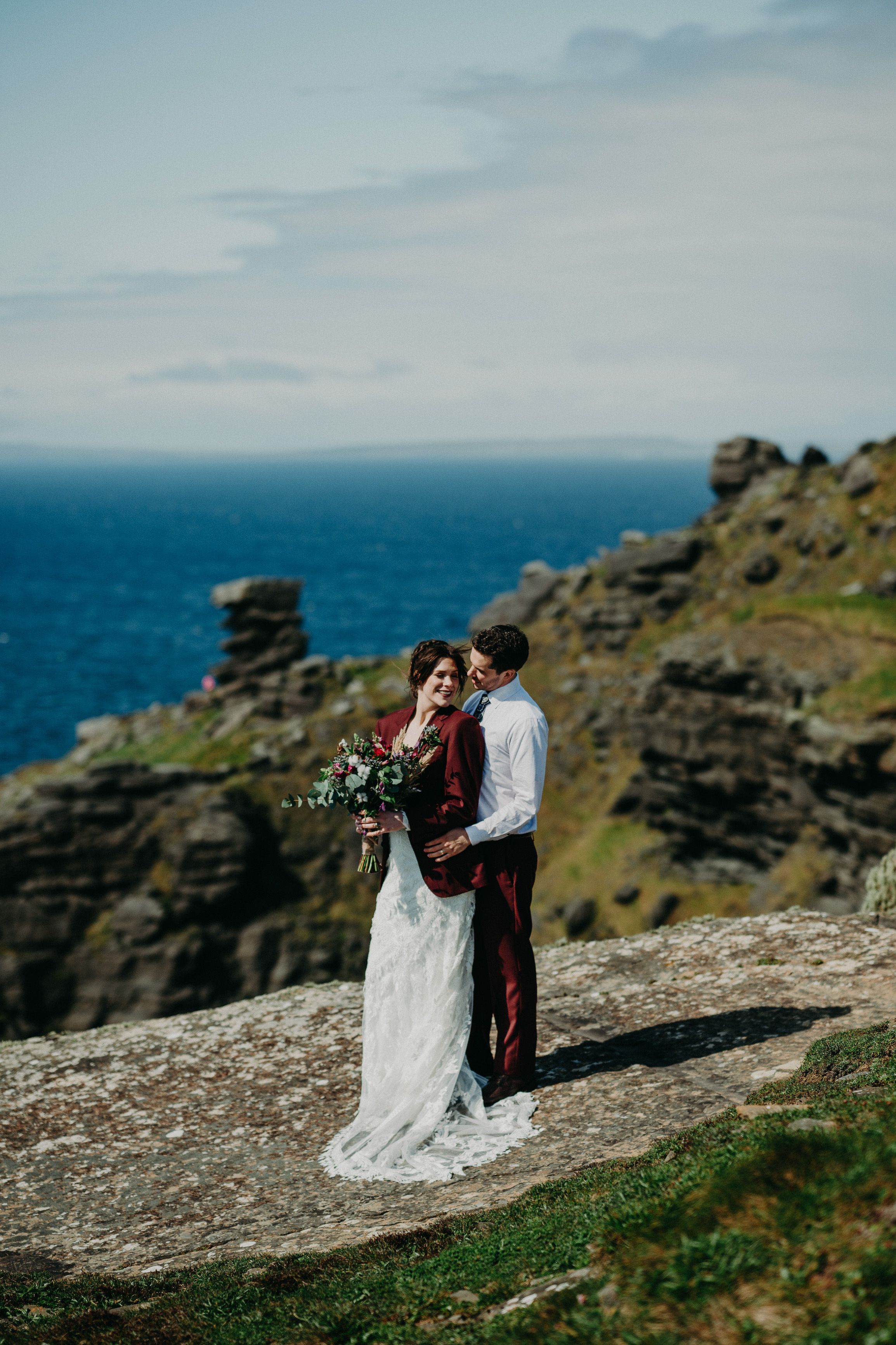 A bride and groom with a majestic view of the sea while they stand on top of a cliff after their smallwedding in Ireland
